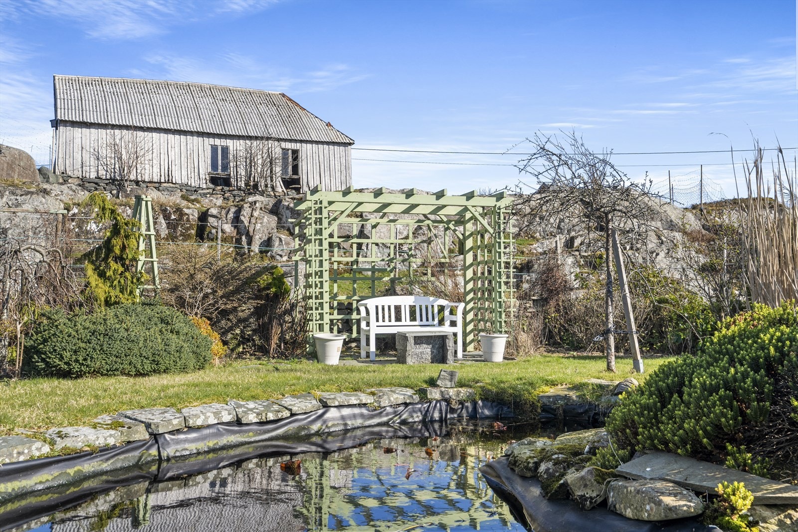 Uteplass ved hagedam. Det er eit rikt utval av plantar på eigedomen. Galleribilde