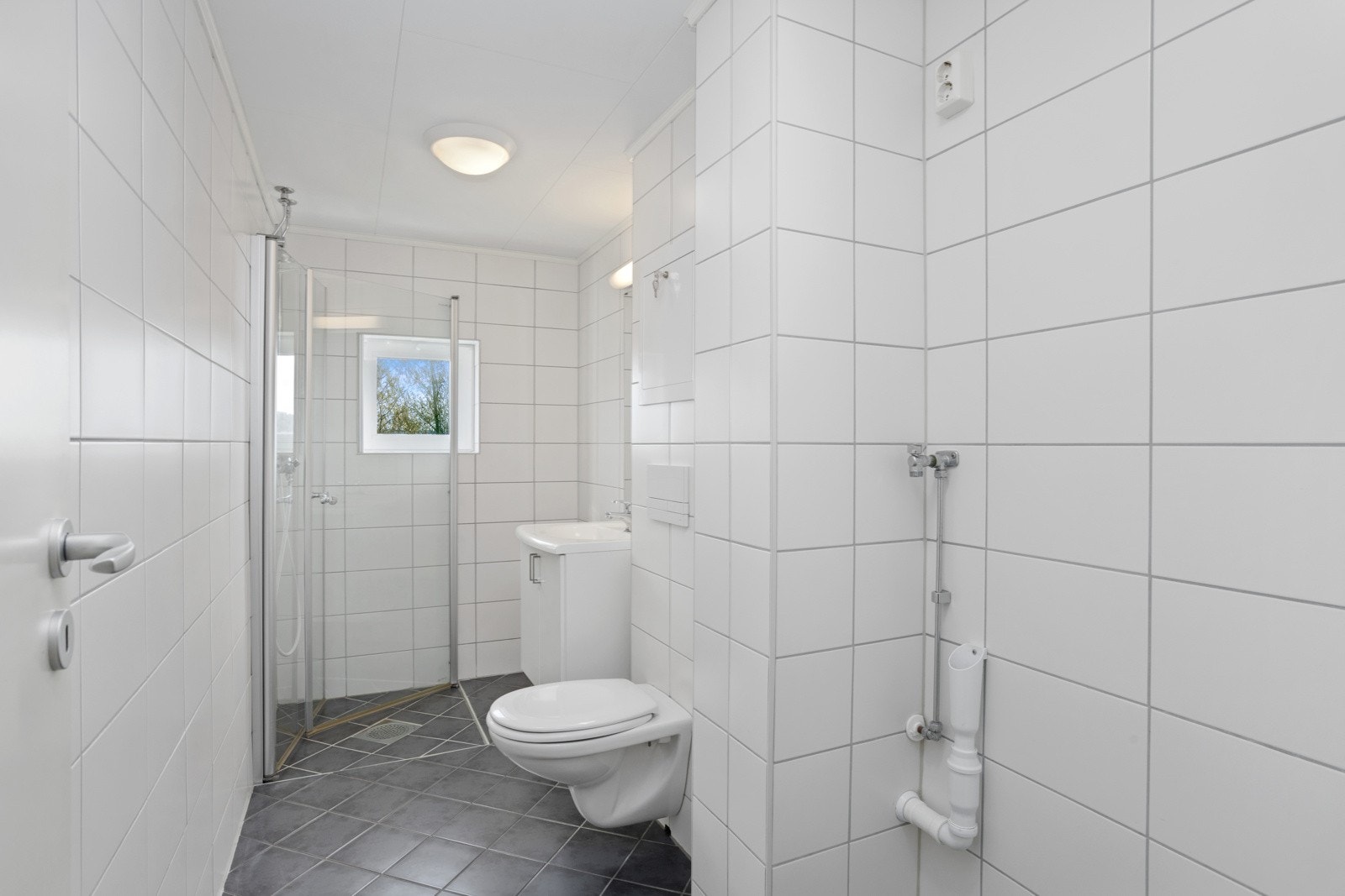 Badet er pent, lyst og flislagt med vegghengt toalett og plass til vaskemaskin. Galleribilde