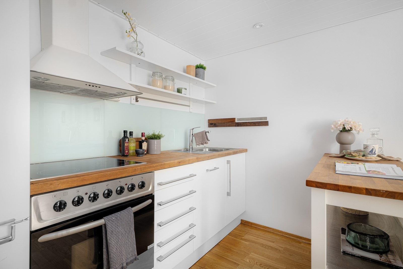 Kjøkkeninnredning fra 2008 med glatte folierte fronter, benkeplate i tre med nedfelt kum i rustfritt stål, glassplater på vegg over benk og ventilator med kullfilter. Galleribilde