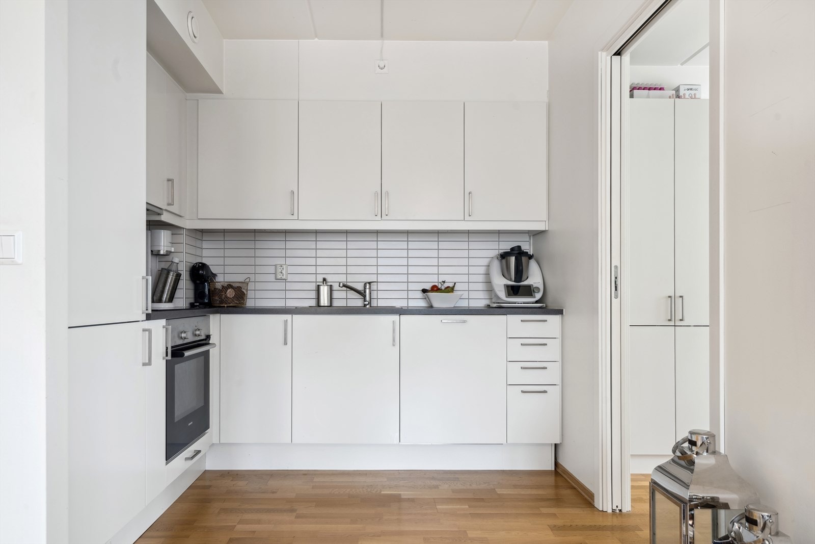 Flott kjøkkeninnredning med hvite glatte fronter, benkeplate av laminat og kjøkkenkum. Galleribilde