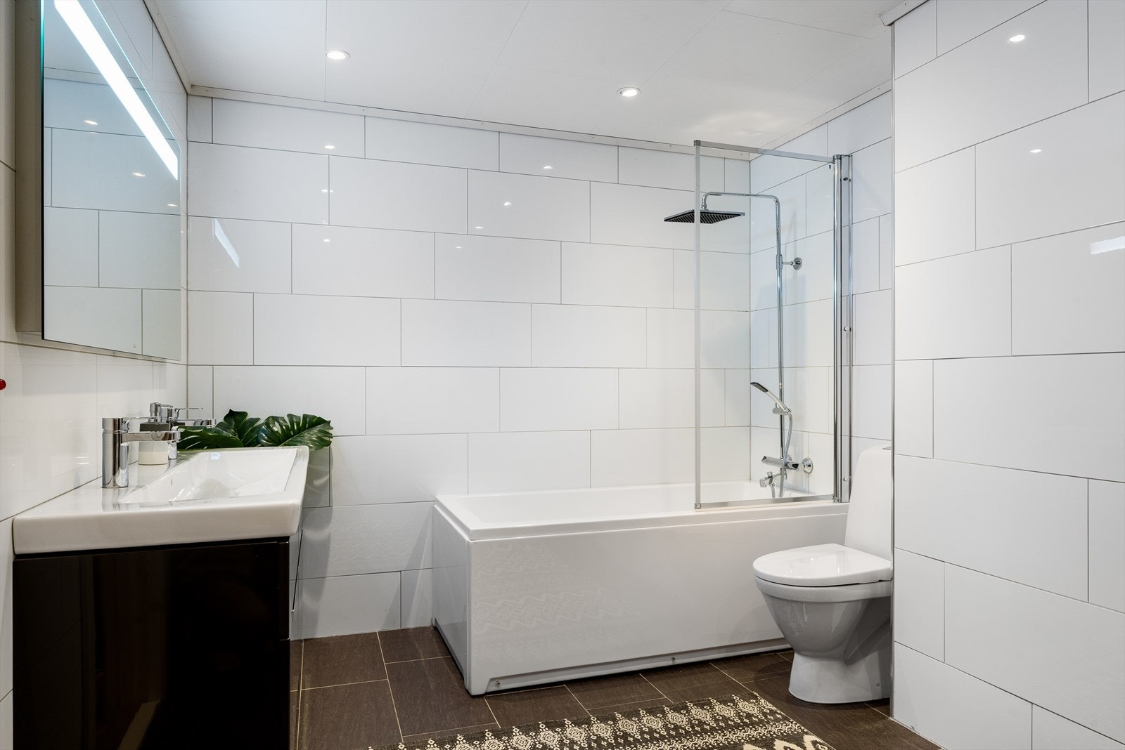 Baderommet i underetasjen fremstår som funksjonelt og innbydende, med flislagte vegger og gulv samt elektriske varmekabler som gir behagelig varme. Taket er utstyrt med Takess-plater og downlights som sørger for god belysning. Galleribilde