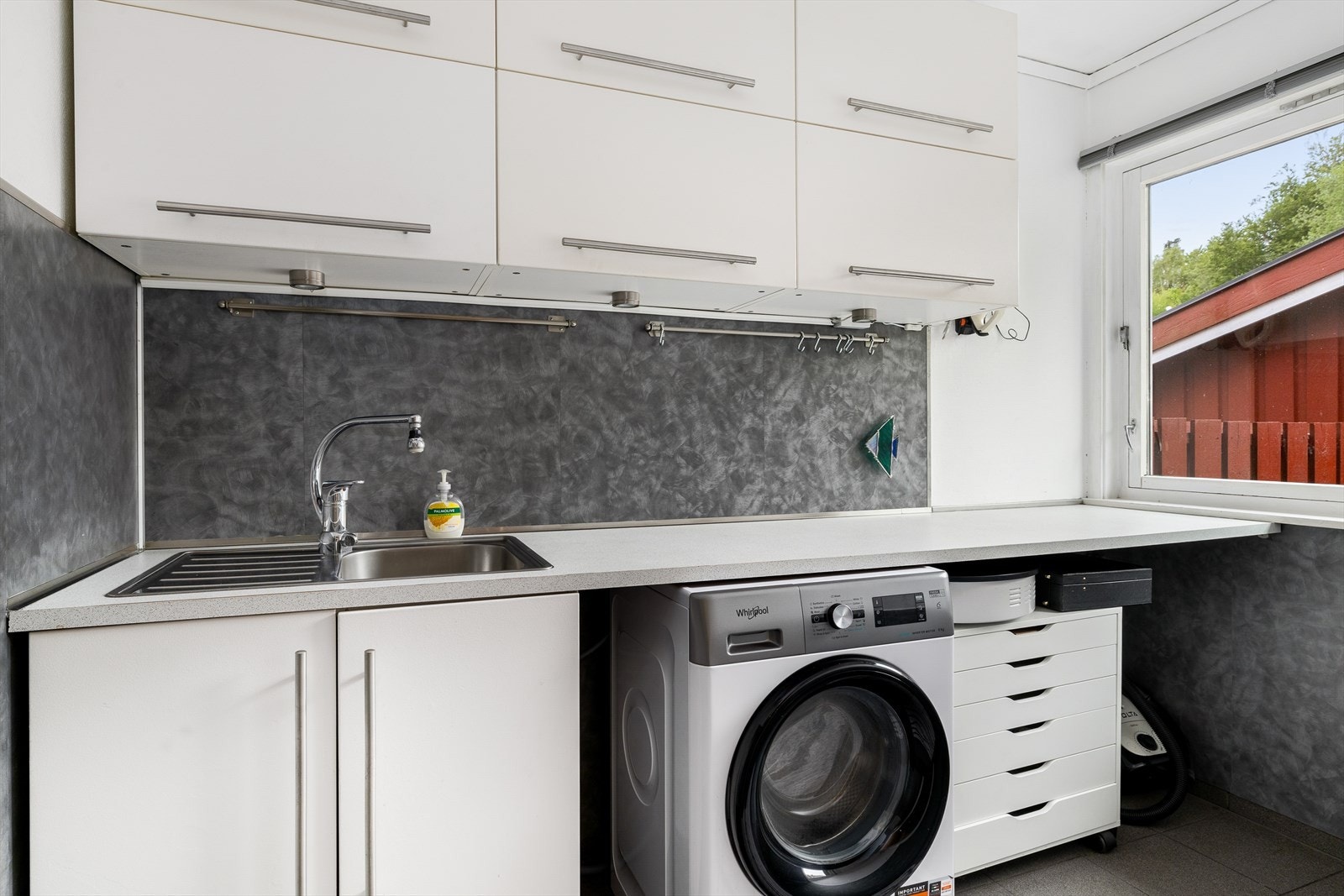 Vaskerommet er praktisk innredet med flislagt gulv og oppkant, samt vegger med en kombinasjon av fliser, plater og malt tapet. Taket har malte plater som gir et rent og enkelt uttrykk. Galleribilde