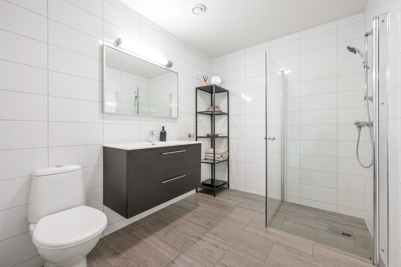 Flislagt bad innredet med servant i møblement og dusjhjørne. Galleribilde