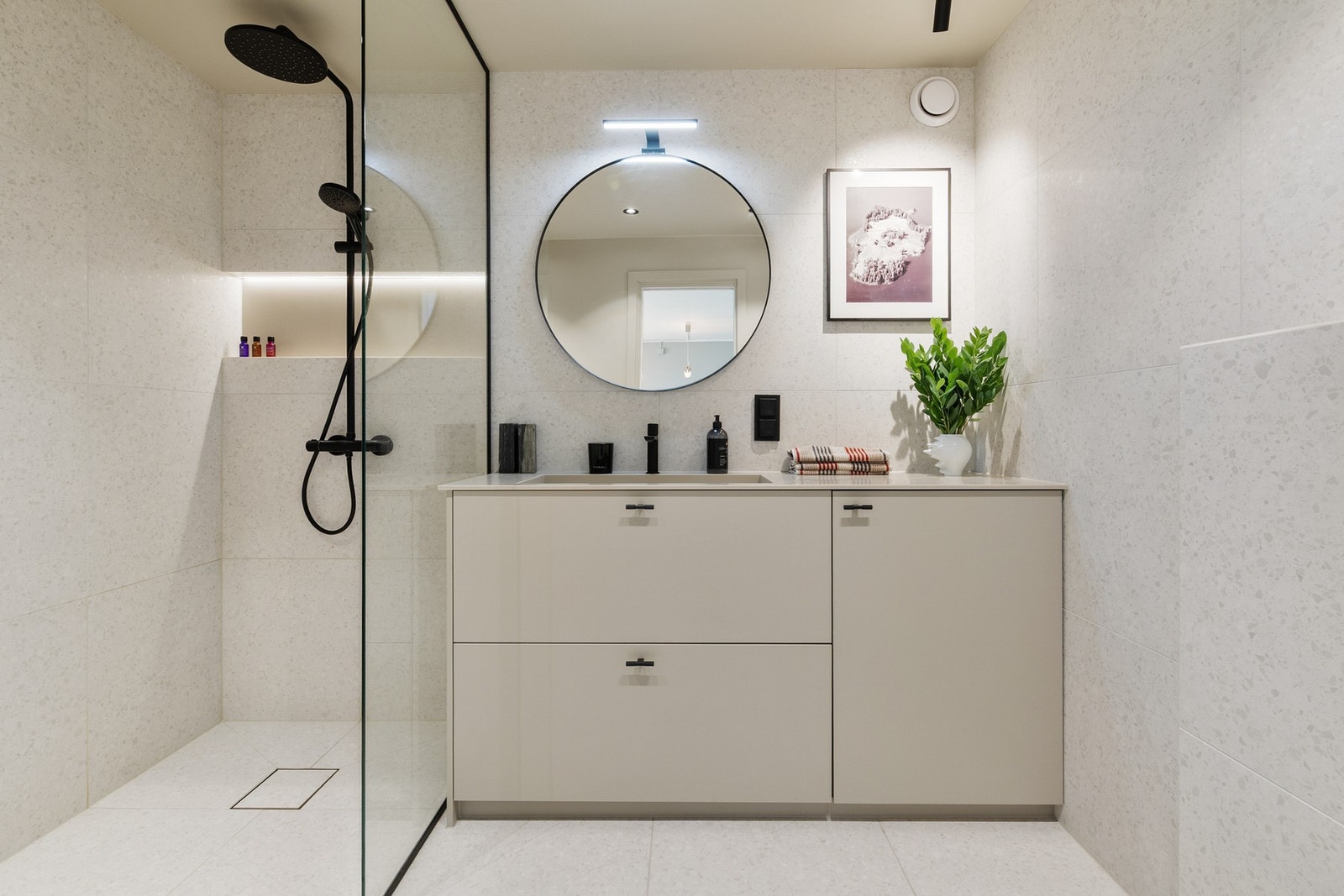 Badet er innredet med benkeskap med benkeplate av Corian, speil på vegg, overlys, vegghengt toalett med innebygd sisterne og dusjsone med innfellbare glassdører, regnfallsdusj og hånddusj. Galleribilde