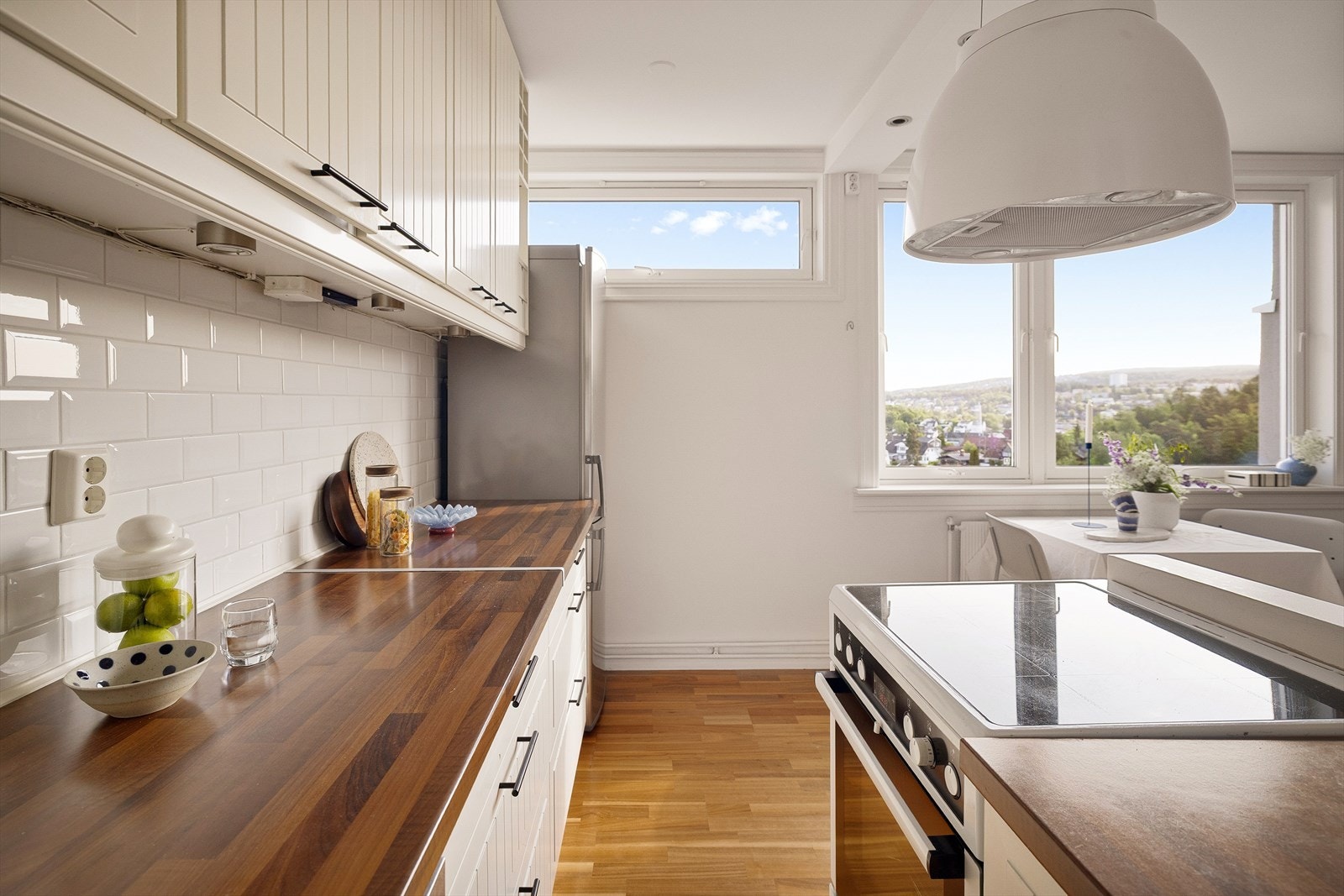 Innredningen består av hvite profilerte fronter, laminat benkeplate og nedfelt oppvaskkum i rustfritt stål. Hvite, pene fliser over benken gir et rent og tidløst uttrykk. Galleribilde