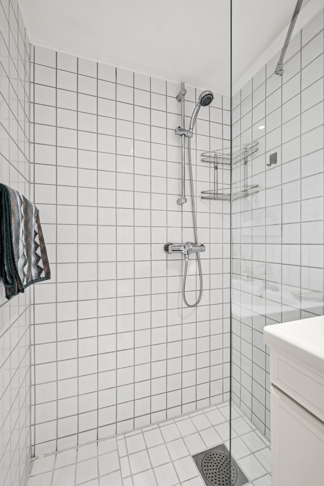 Innredning består av servant med underskap, speil med overlys, gulvmontert toalett og et dusjhjørne med fast glassvegg. Galleribilde