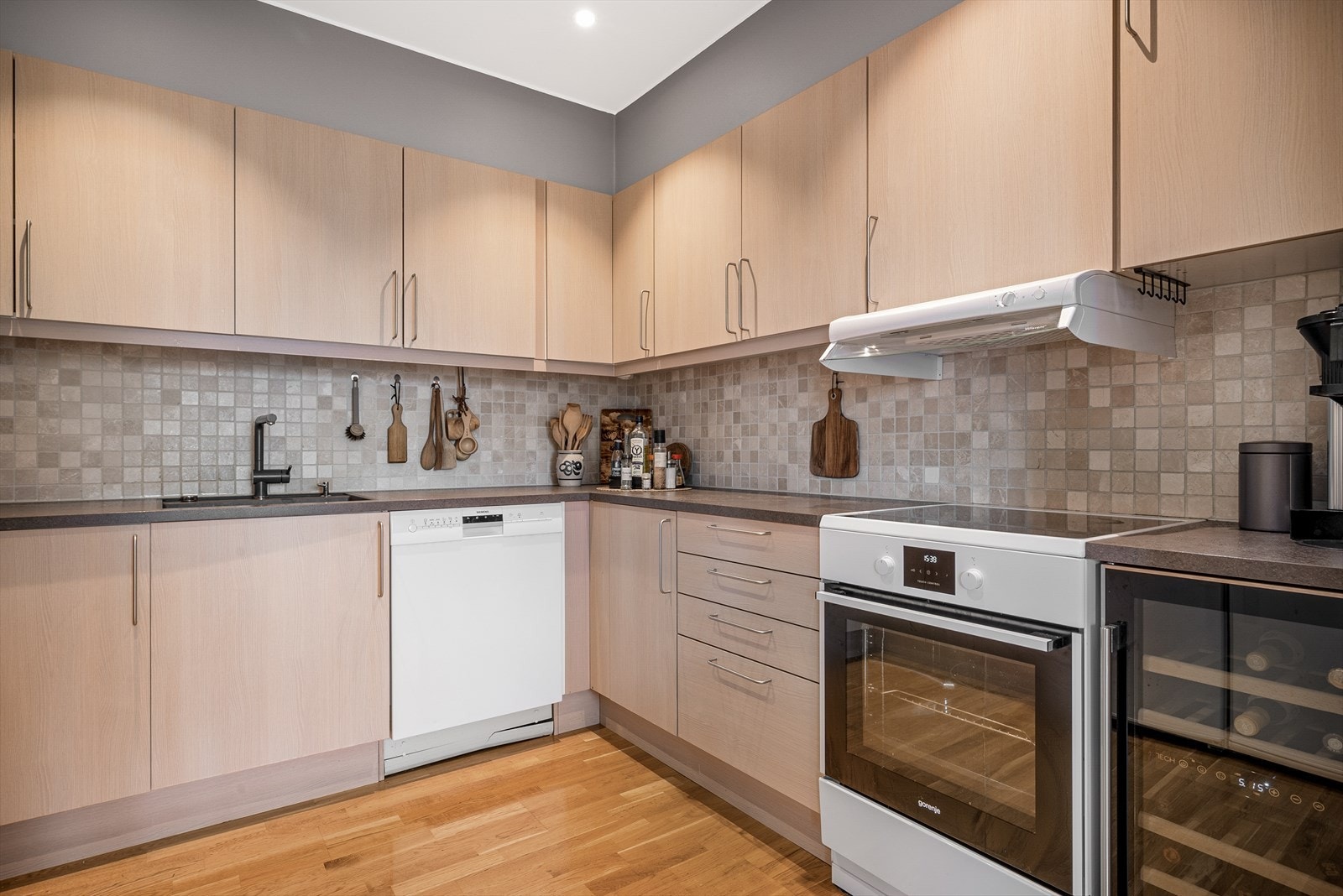 Kjøkkenet er moderne og har parkett på gulv, malt overflate og flis på vegg over benkeplate Galleribilde