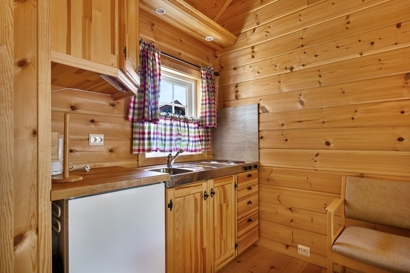 Liten kjøkkeninnredning av heltre, med heltre benkeplate. Kombinert oppvaskkum med kran og kokeplate med benk i stål. Galleribilde