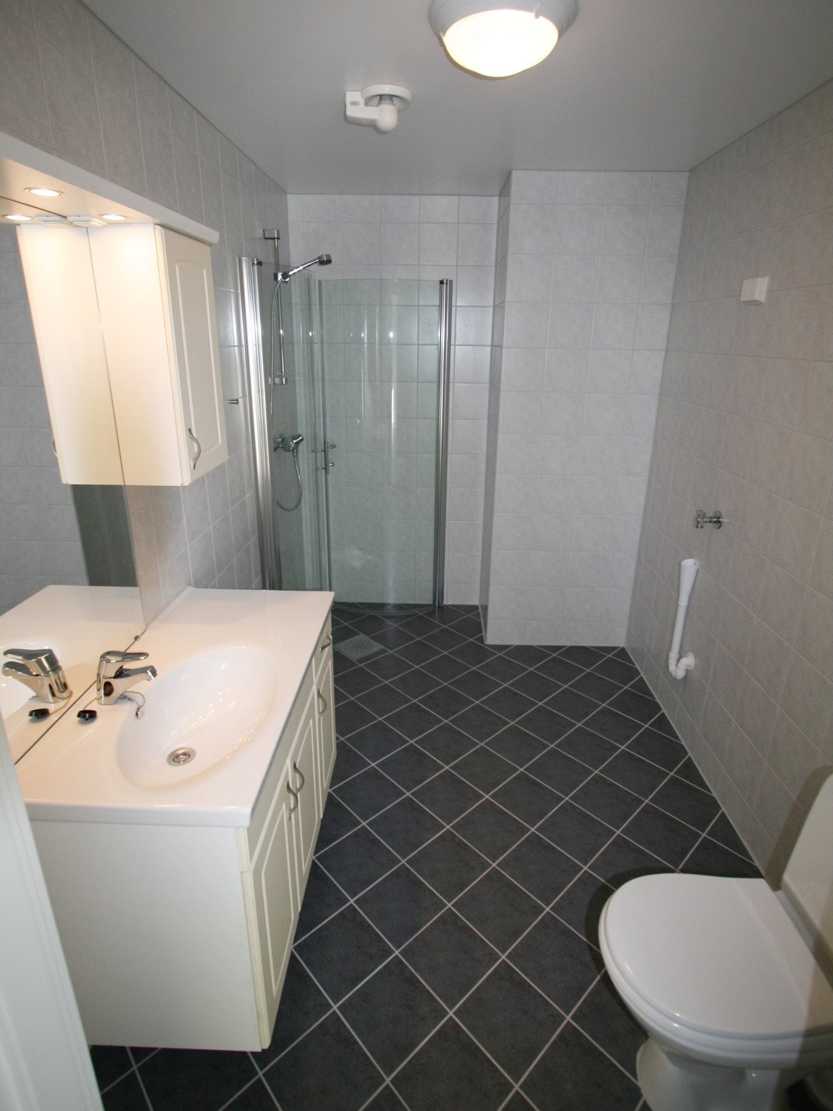 Badet er innredet med servantskap med nedfelt servant, gulvstående toalett, dusjhjørne med svingbare glassdører og opplegg for vaskemaskin. Galleribilde