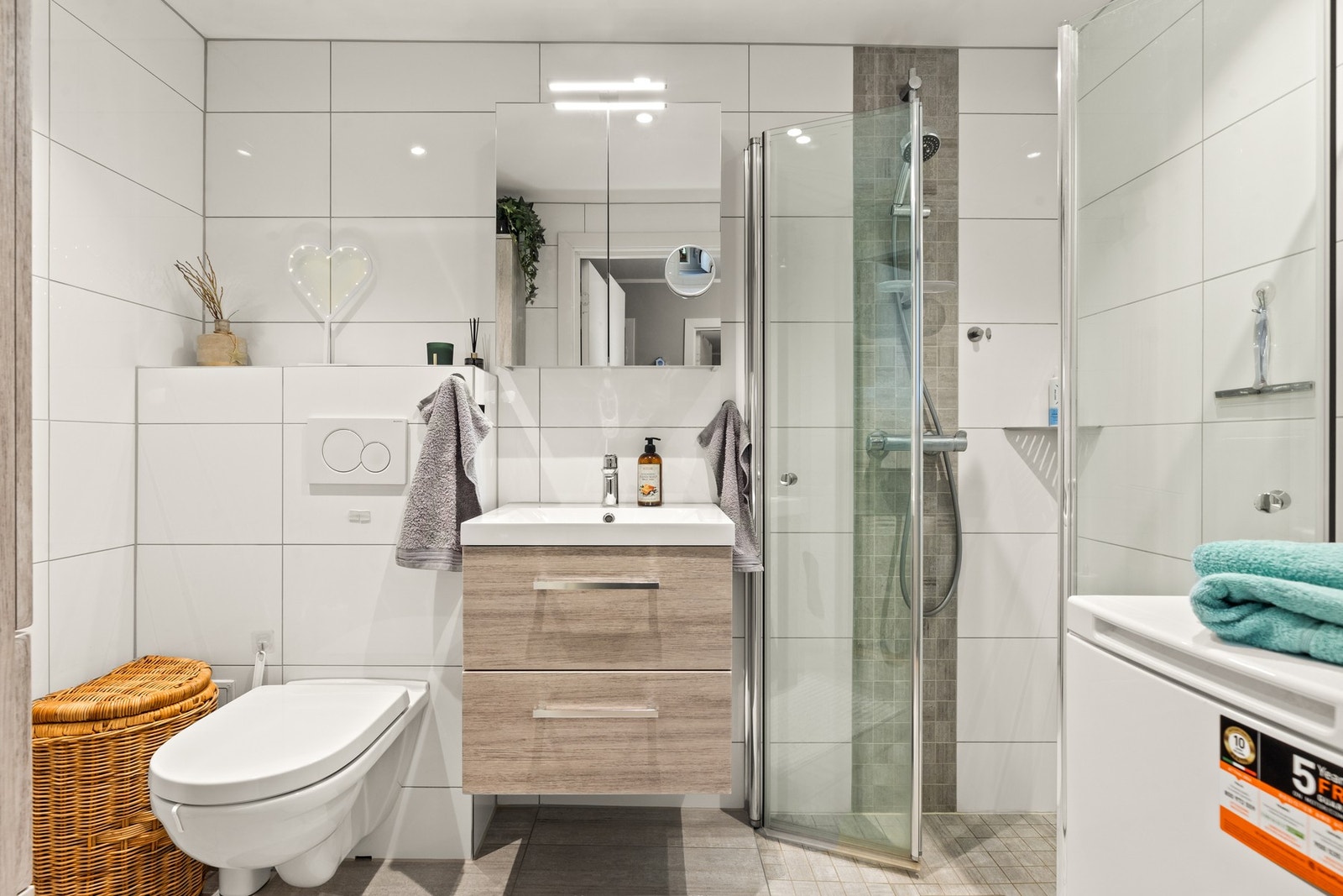 Badet er utstyrt med elektriske varmekabler i gulv, vegghengt toalett, servantskap, speilskap, høyskap, dusjhjørne og opplegg for vaskemaskin Galleribilde