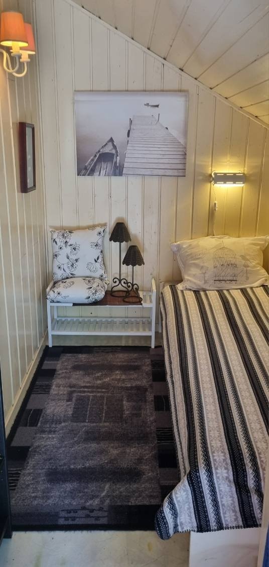 Ved hyttas inngangsparti er det også tilkomst inn til en utebod, som er innredet med en enkeltseng (ikke byggesøkt). Panelte veggflater og himling er malt/beiset i en lys fargetone. Galleribilde