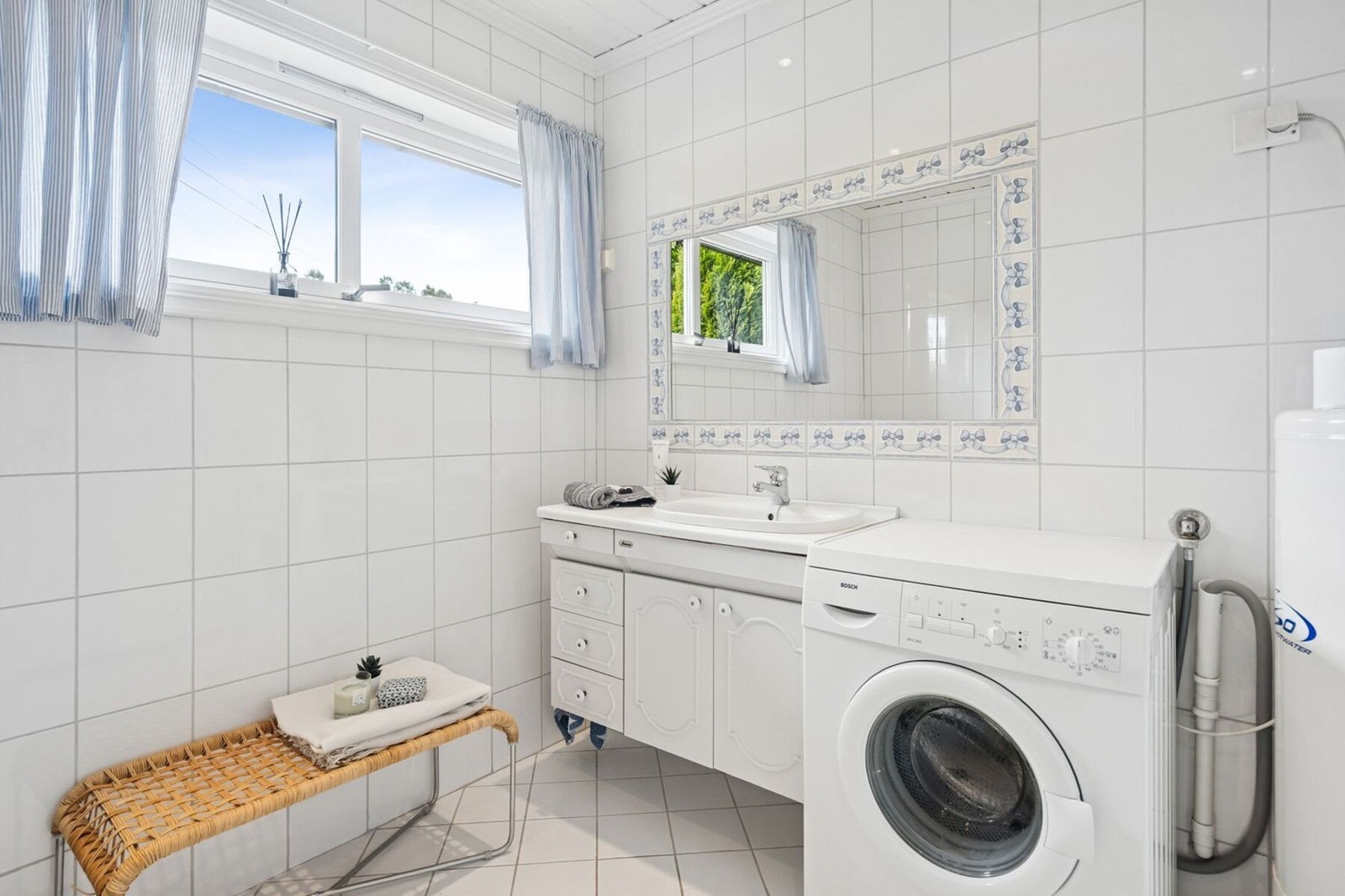 Det lyse badet fra 2004 har hvite fliser på vegg og gulv, samt panel i tak. Rommet har innredning med nedfelt servant, et toalett, dusjvegger/hjørne og det er opplegg for vaskemaskin. Galleribilde