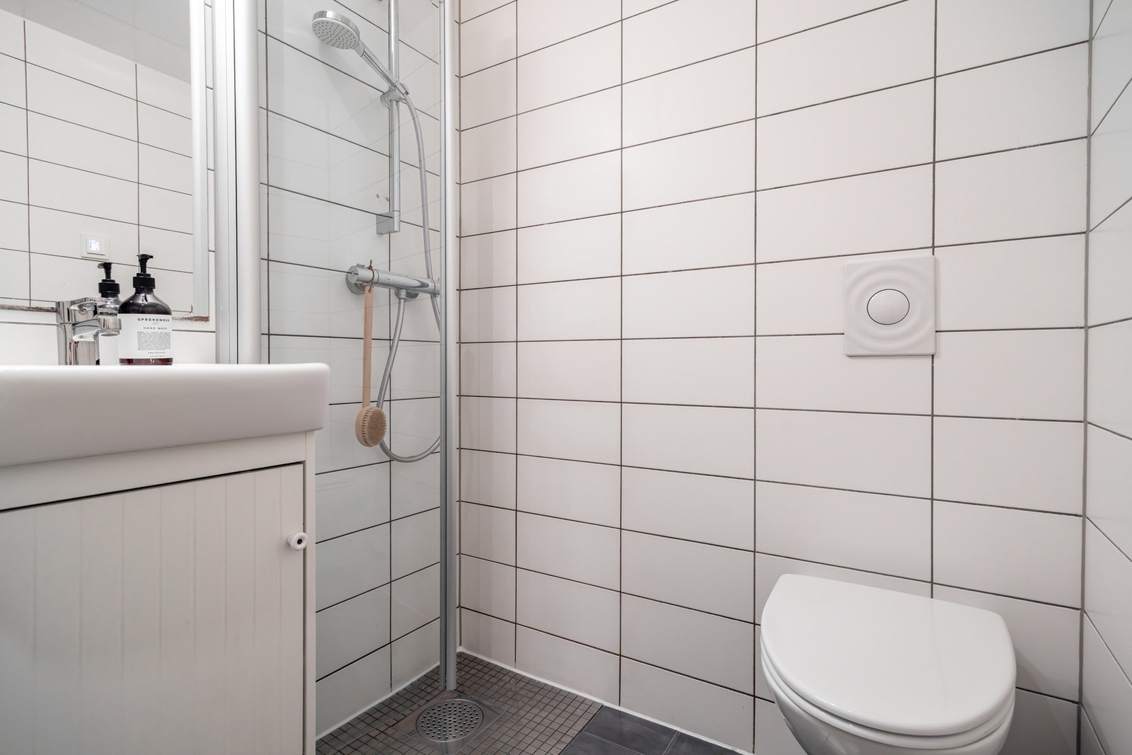 Inneholder servant med skap, speil med belysning, dusjhjørne med glassdør, veggmontert høyskap og vegghengt klosett. Galleribilde