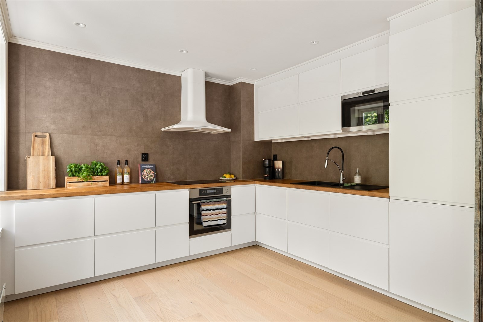 Stilrent kjøkken med moderne innredning og slette hvite fronter som gir et tidløst uttrykk. Kjøkkenet er komplett med integrerte hvitevarer: induksjonstopp, stekeovn, oppvaskmaskin og kombiskap (kjøl/frys). Galleribilde