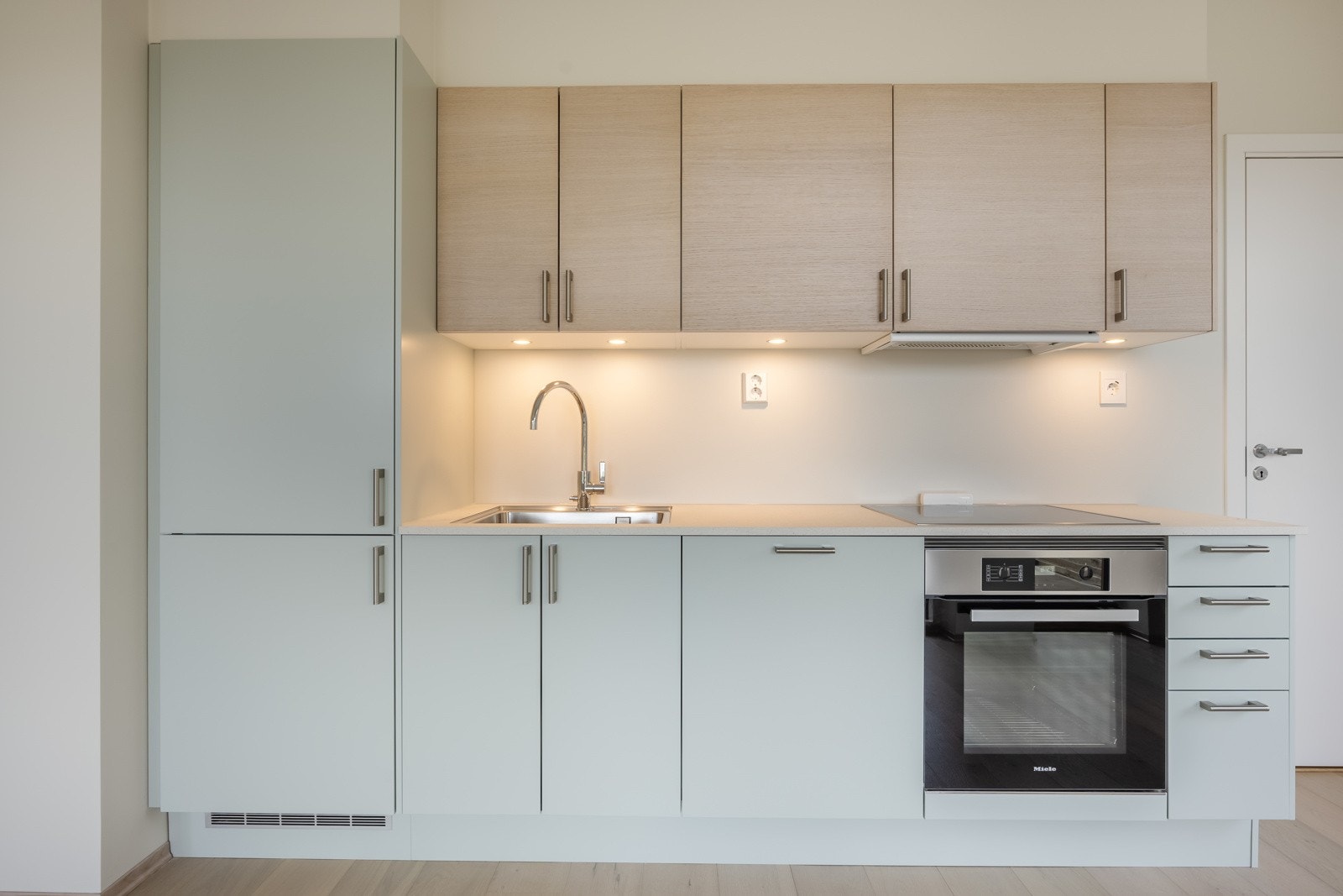 Kjøkkeninnredningen er i en lys dempet grønnfarge i kombinasjon med overskap i eikefiner. Galleribilde