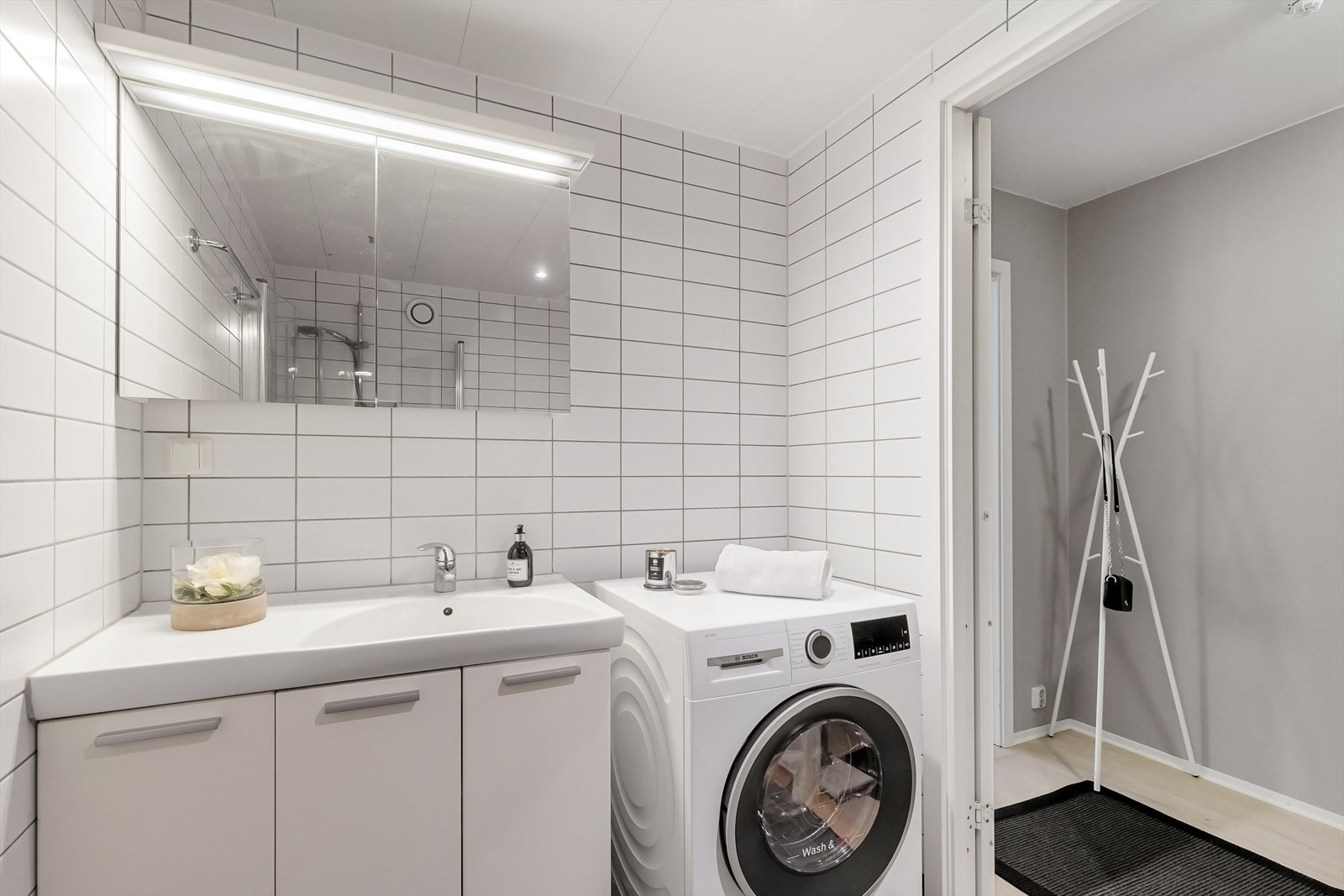 Servantinnredning med skap, veggmontert toalett, speilskap med belysning og opplegg for vaskemaskin. Galleribilde