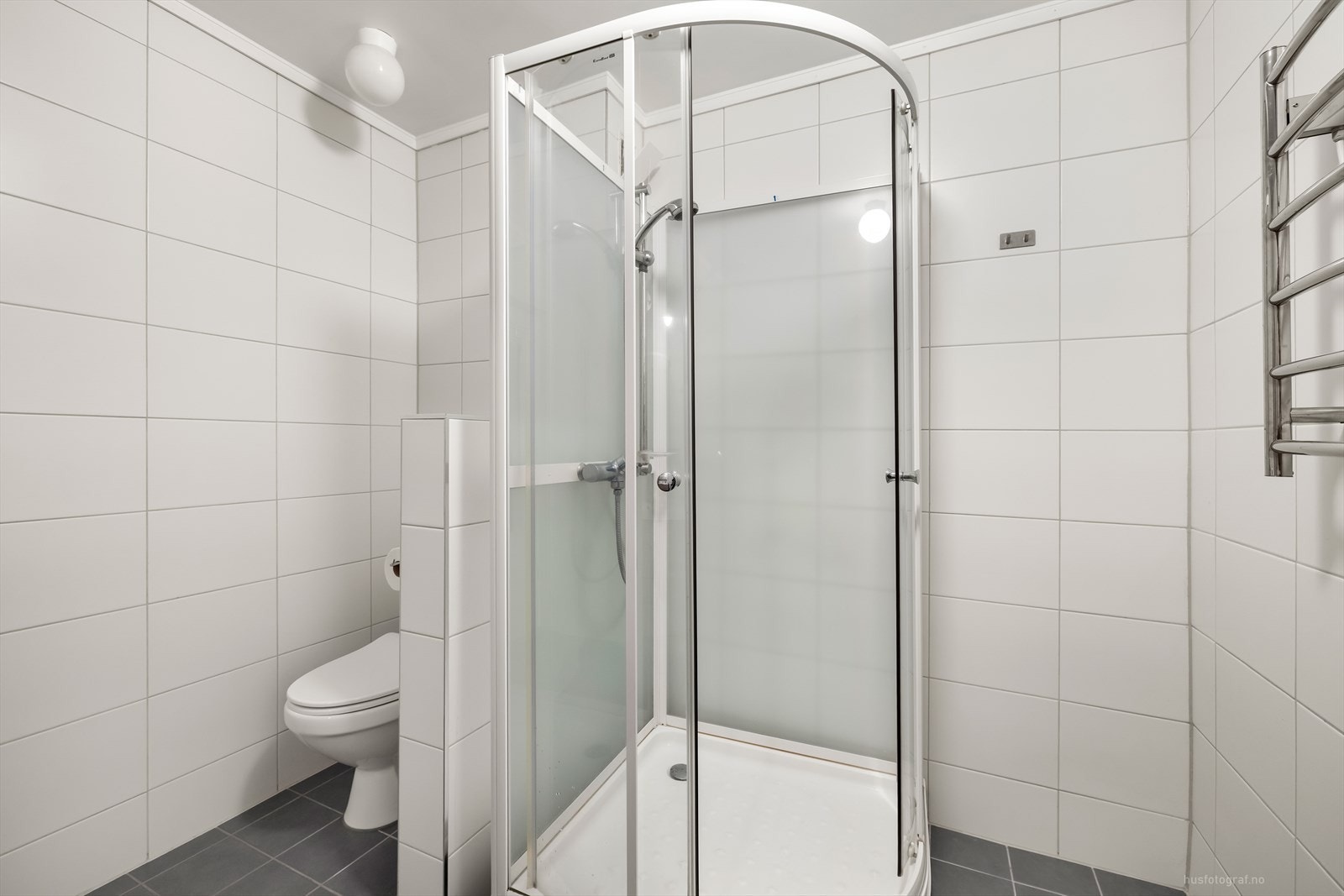 Lyst og pent baderom med dusjkabinett og håndkletørker montert på vegg. Galleribilde