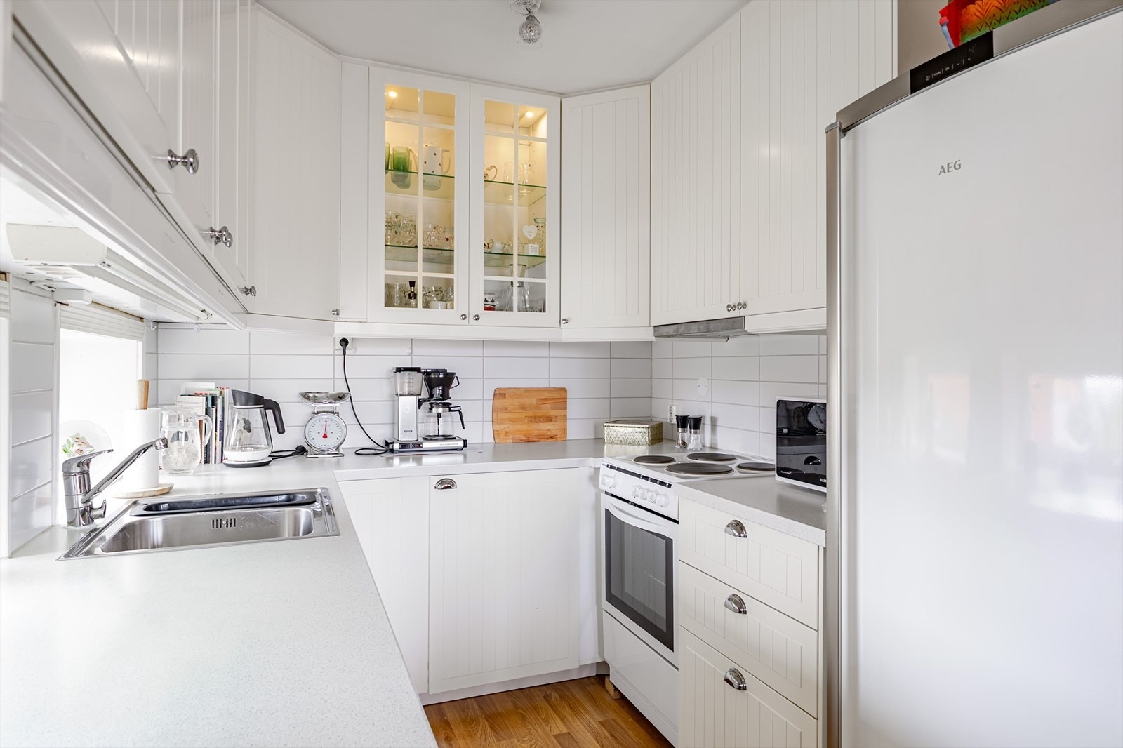 Lys kjøkkeninnredning med profilerte fronter og fliser på vegg mellom overskap og benkeplate. Galleribilde