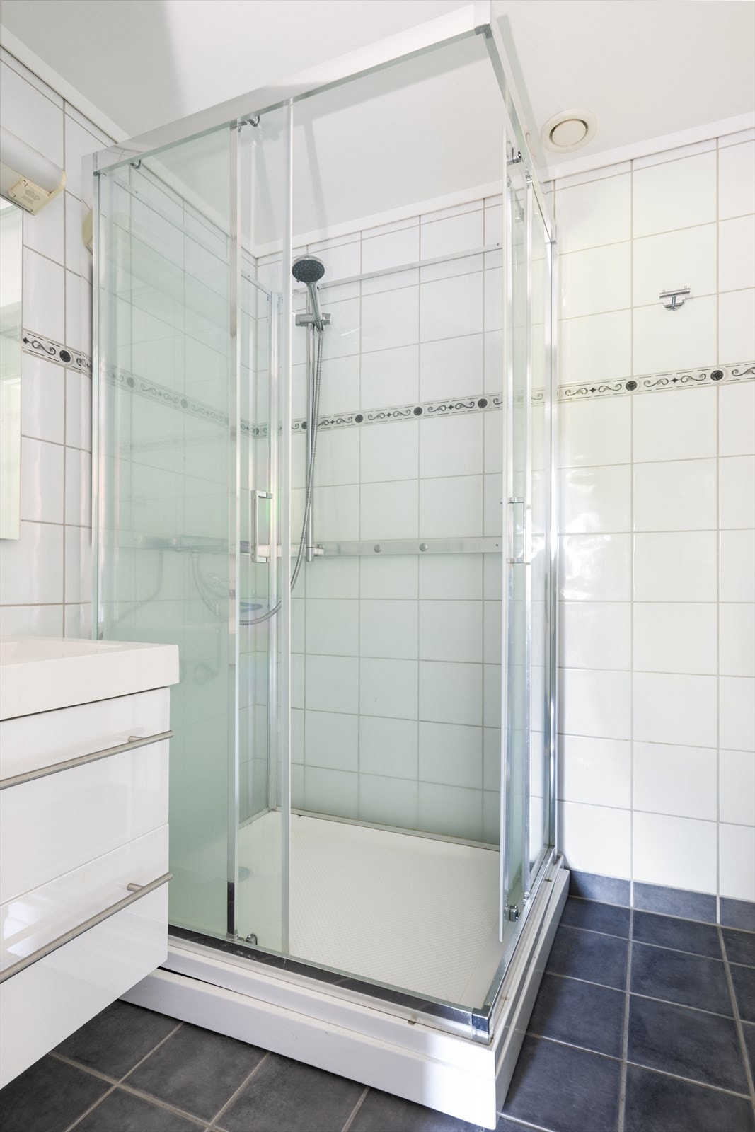 Baderom har overflater bestående av flis på vegger, flislagt gulv med elektriske varmekabler samt malte slette flater i himling. Lys slett baderomsinnredning med skuffer og heldekkende servant. Over innredningen er det speilflate med lys over. Galleribilde