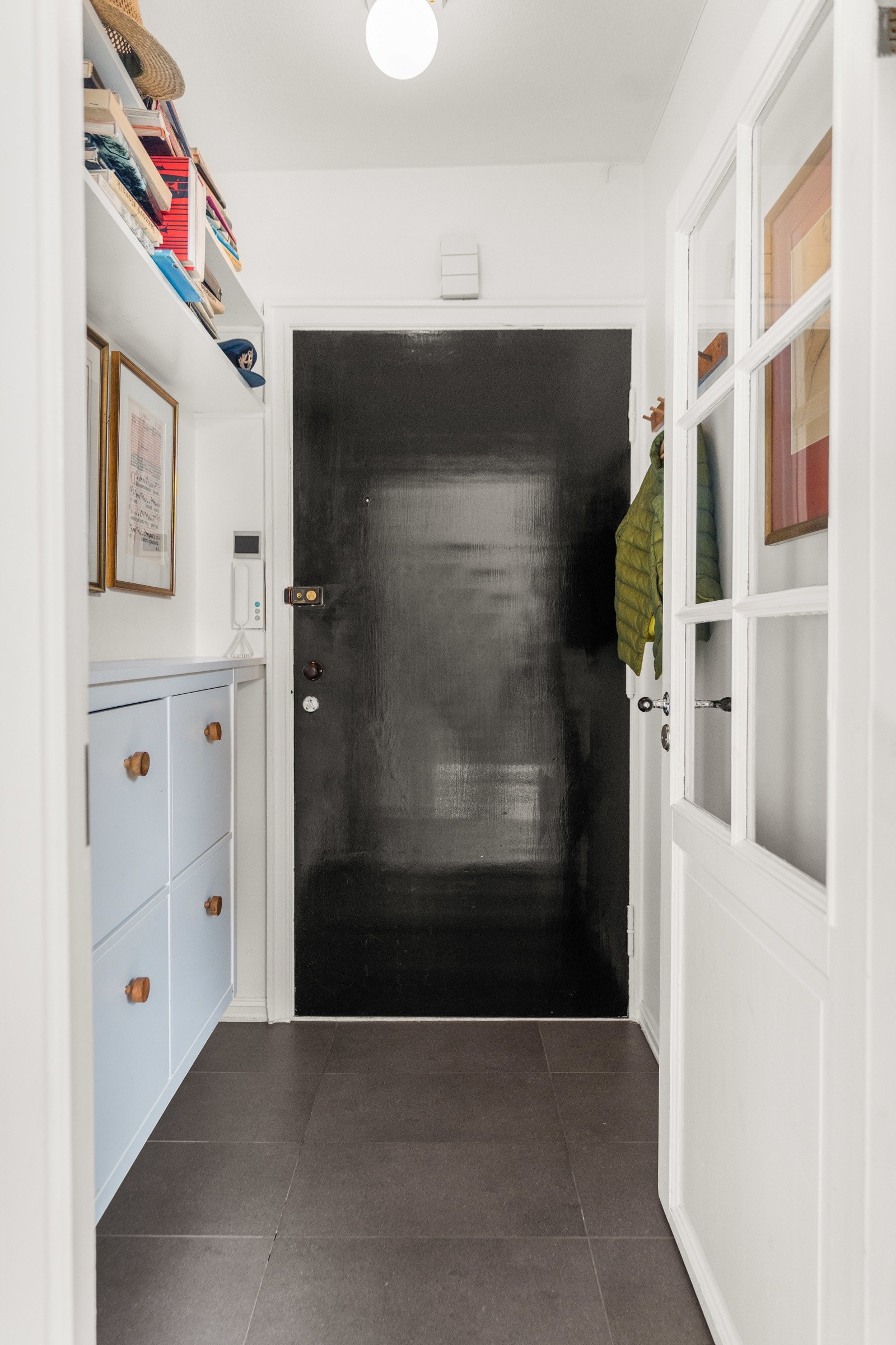 Trivelig entré med plass til yttertøy samt hyller og skapløsning. Mørke gulvfliser og sjarmerende dør med sprosser videre inn til neste rom i leiligheten. Galleribilde