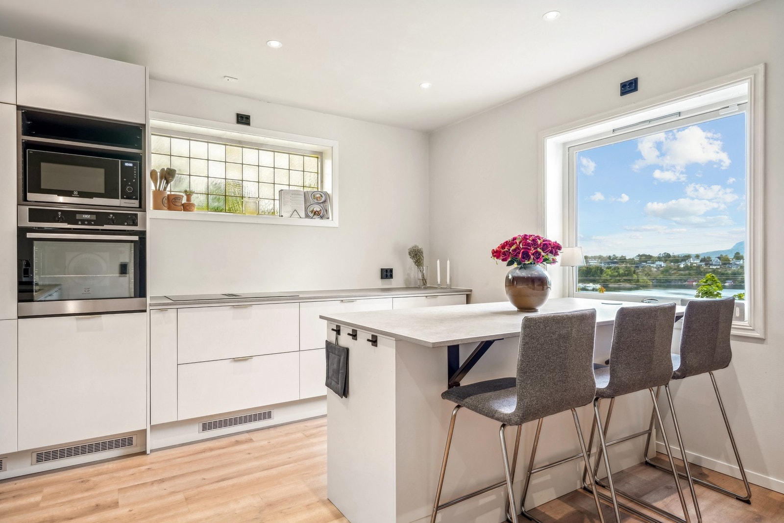 Stilfull kjøkkeninnredning med hvite, glatte fronter og keramikk benkeplate. Her finner du integrert kjøleskap, oppvaskmaskin, platetopp og stekeovn. Galleribilde