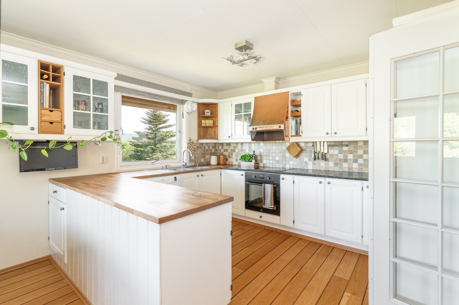 Kjøkken har lys innredning med profilerte fronter, og benkeplate av heltre og steinkompositt med flis over. Galleribilde