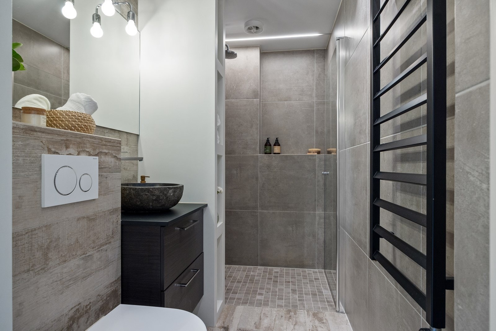 Delikat bad med flislagte vegger og gulv med varmekabler som gir en behagelig temperatur. Vaskemaskin er installert på kjøkken. Galleribilde