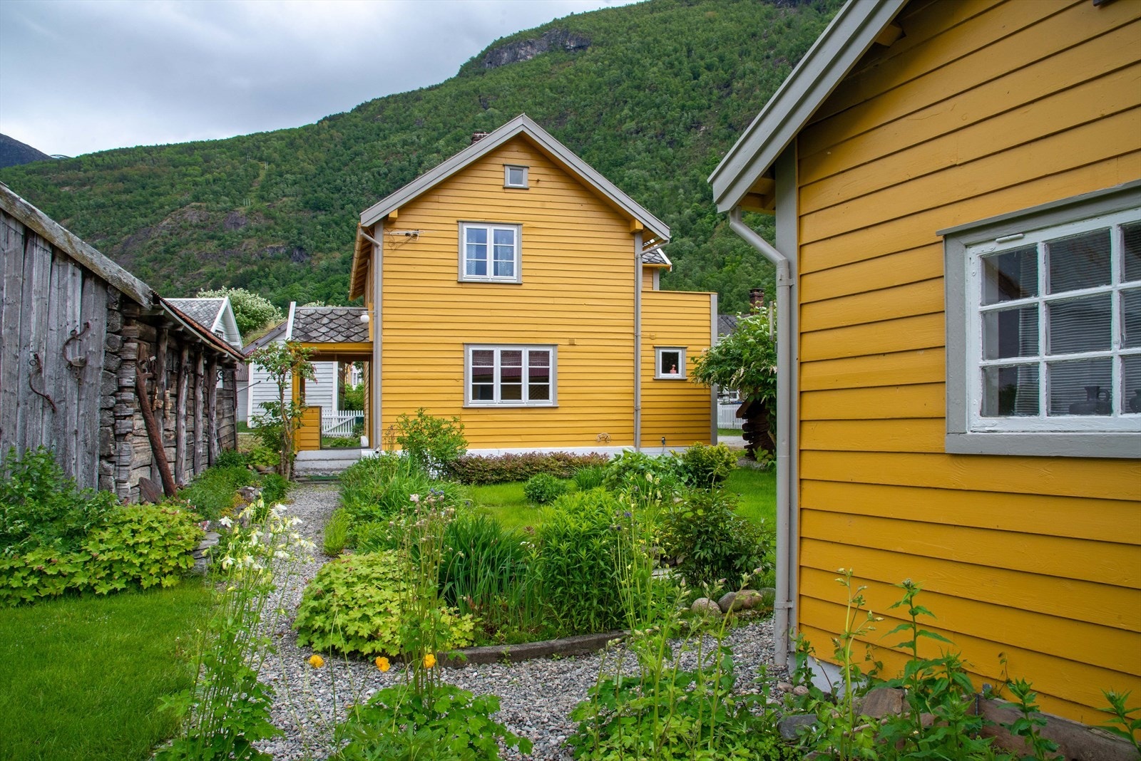 Baksida av bustaden er opparbeida med plen og planter, gruslagte gangbaner, steinlagte stiar, stakittgjerde og bedd med blomster. Galleribilde