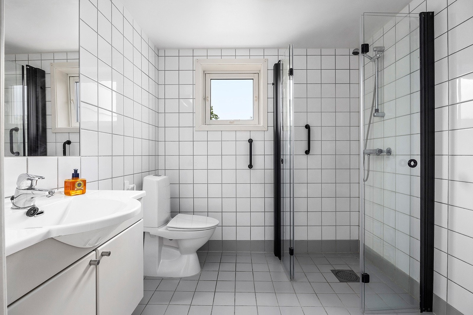 Flislagt bad med varme i gulv. Badet inneholder dusjhjørne med inn-/utadslående dører, toalett, baderomsmøbel med servant og innlimt speil med belysning. Det er opplegg for vaskemaskin. Galleribilde