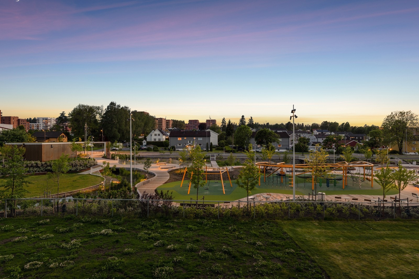 Nyt utsikten på kvelden til Skårerparken med sildrende vann, gangveier, trær, blomster, benker og bord. Galleribilde