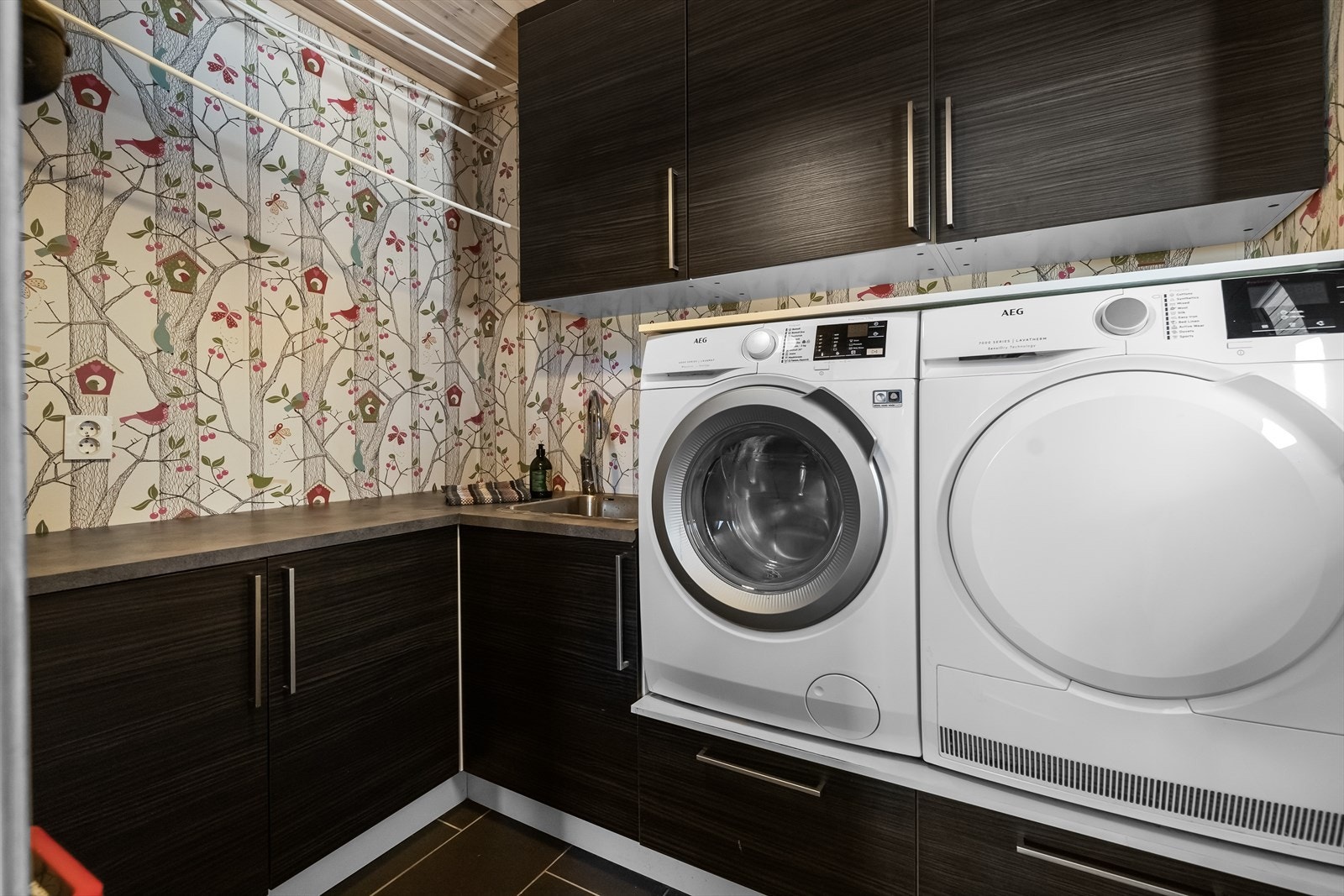 Fra gangen er det direkte inngang til et praktisk og arealeffektivt vaskerom med flislagt gulv, gulvvarme, godt med skap- og benkeplass, nedfelt utslagsvask samt opplegg for vaskemaski, tørketrommel og takhengt tørkestativ. Galleribilde