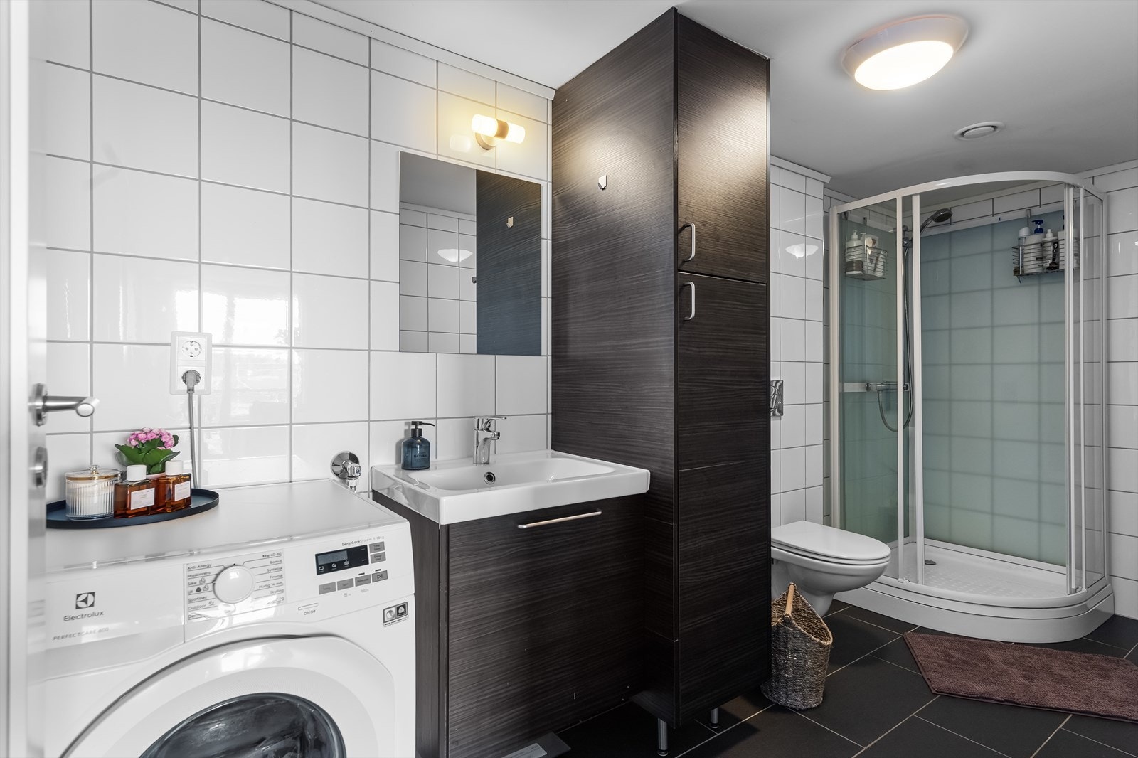 Badet er tidløst og pent med flislagte overflater på gulv og vegger. Badet har dusjkabinett, godt med innredning og servant, vegghengt toalett og opplegg for vaskemaskin. Galleribilde