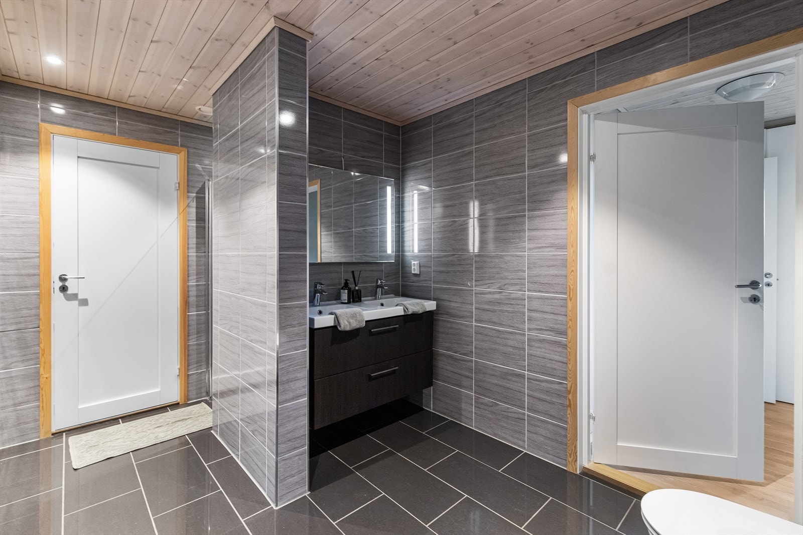 Det er utstyrt med servant i baderomsinnredning, speil med integrert lys, dusjnisje med regndusj og vegghengt toalett. Galleribilde