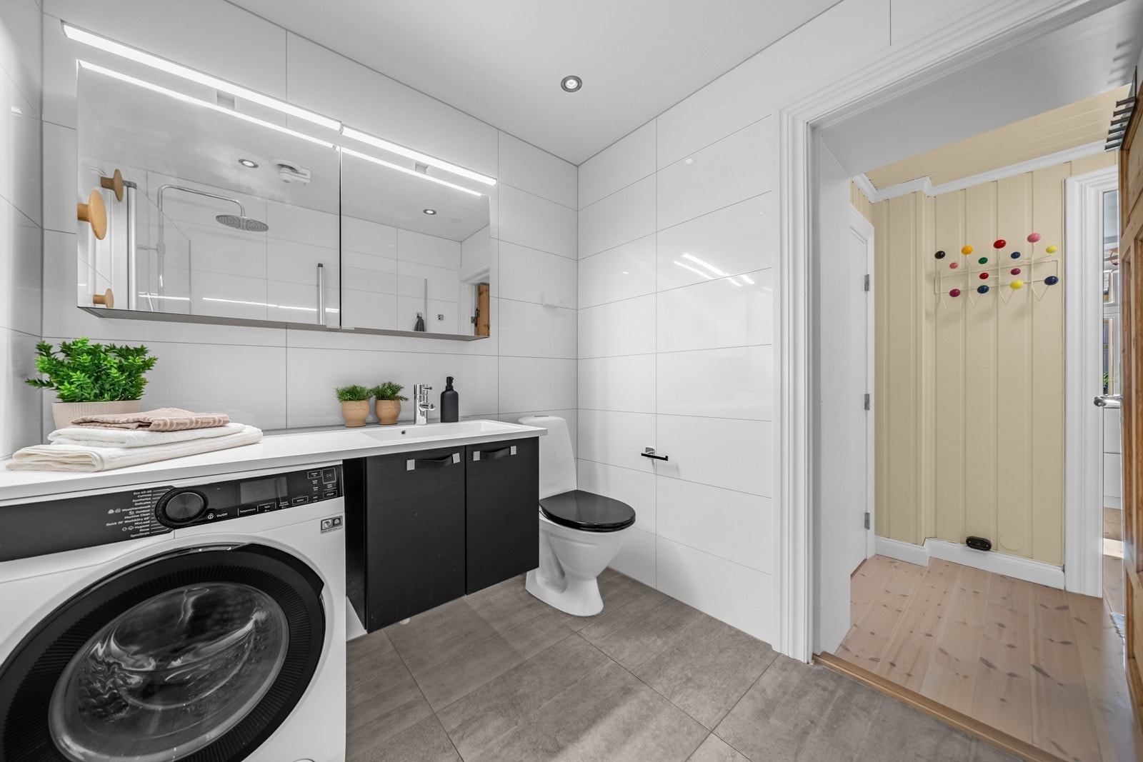 Badet er utstyrt med gulvstående toalett, servantinnredning med servant, ettgreps blandebatteri, speilskap med belysning, blandebatteri/dusjarmatur, dusjdører i glass, plass og opplegg for vaskemaskin. Galleribilde