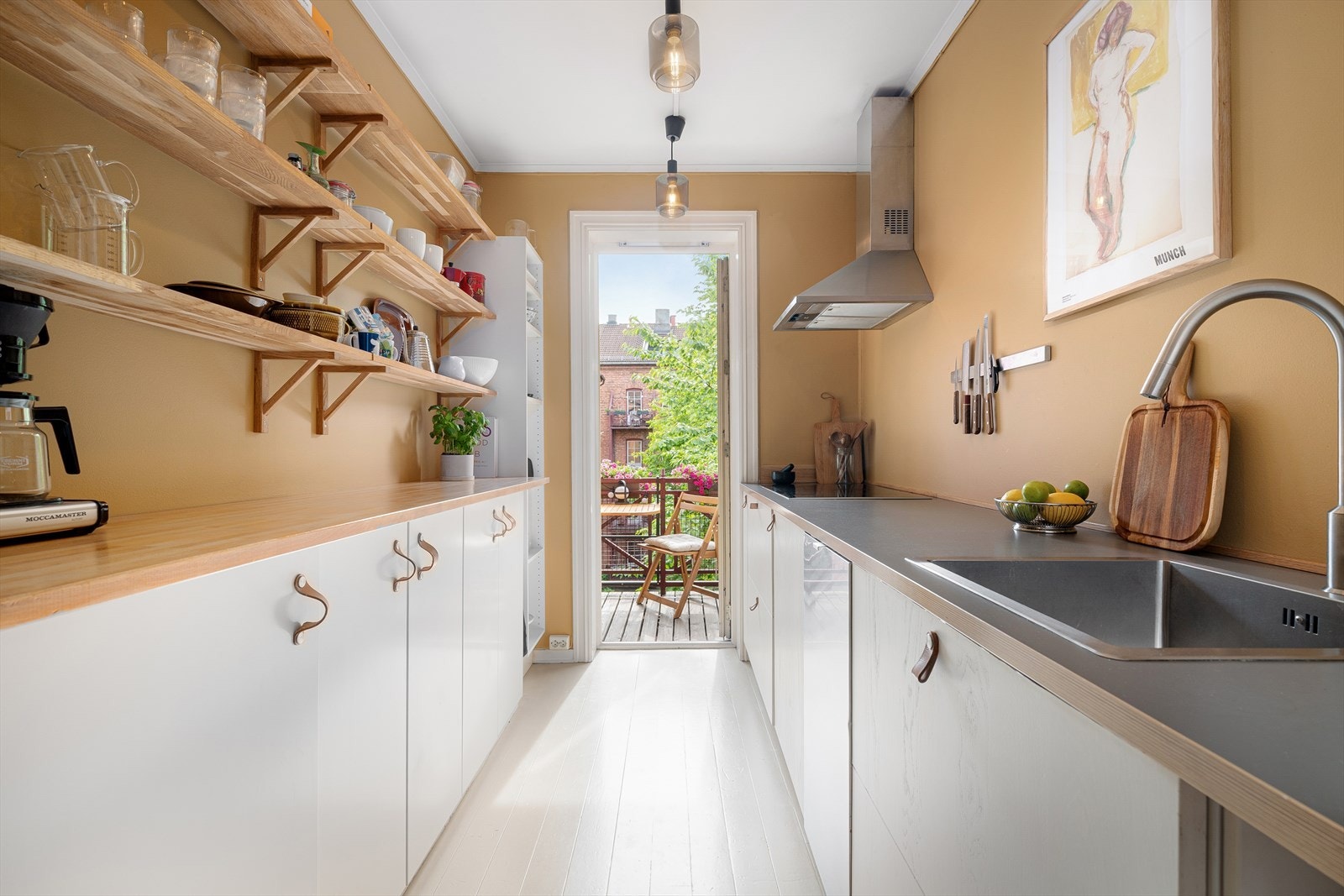 Ved å innrede med få overskap og flere underskap får man mer luft og åpenhet på kjøkkenet. Det er integrert komfyr med induksjons platetopp, oppvaskmaskin og kjøleskap og fryseskap under benk. Galleribilde