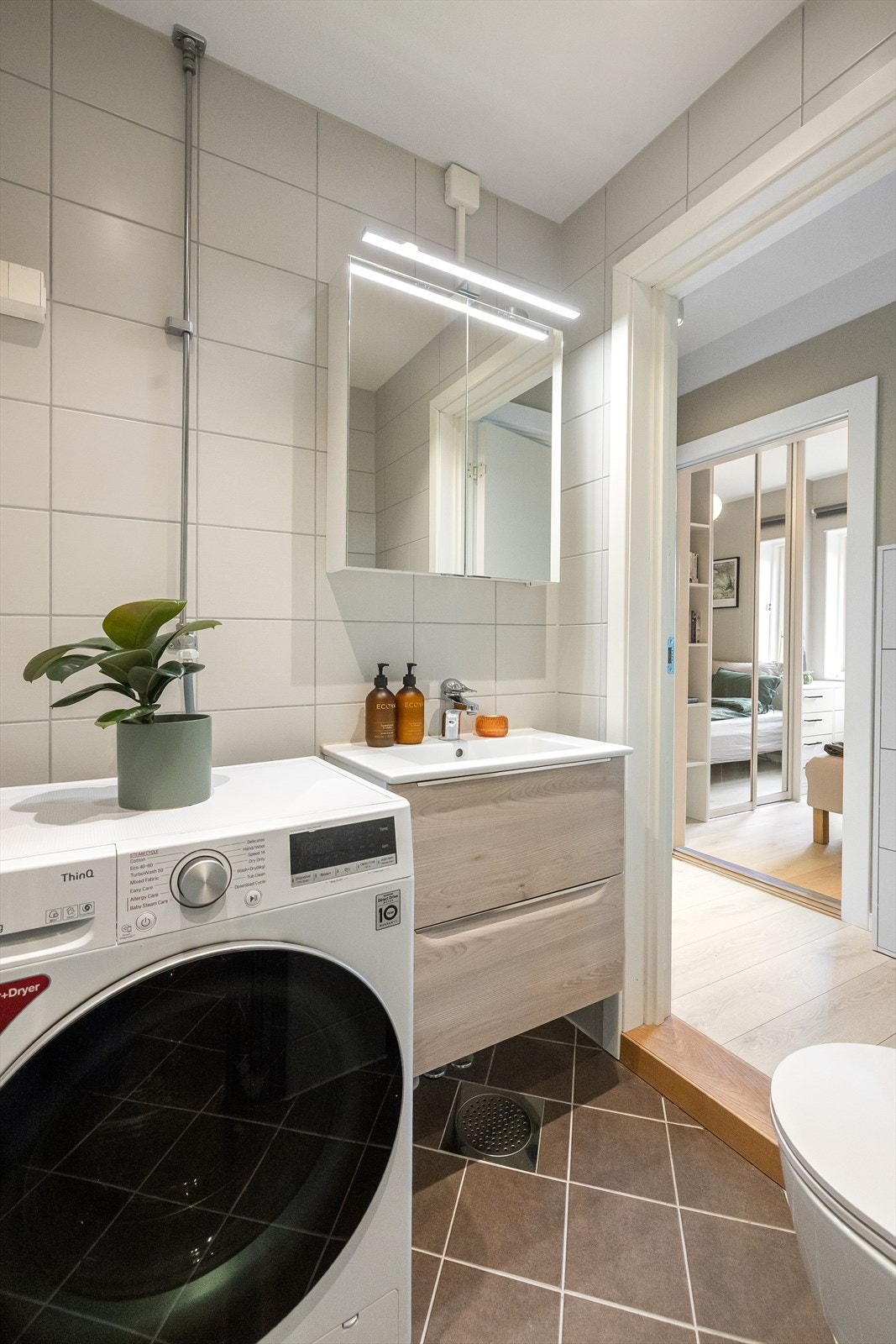 Baderomsinnredning med finerte fronter og heldekkende servant samt speilskap med belysning over. Galleribilde