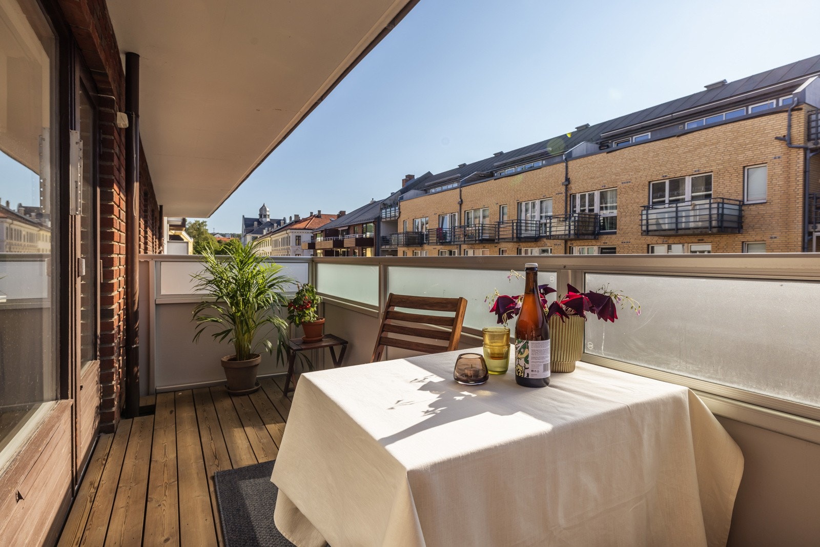 Balkongen er overbygget og har terrassebord på gulvet, samt et stilrent rekkverk med frostede glassfelt som skjermer uten å stjele lys. Galleribilde