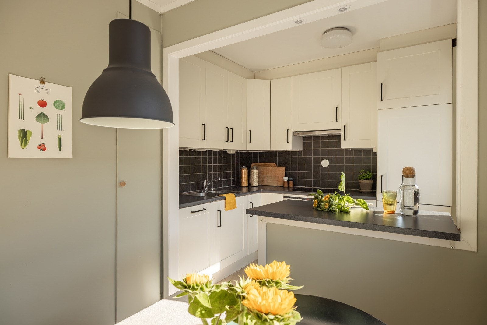 Lys og tidløs innredning med profilerte fronter og laminert benkeplate med nedfelt oppvaskkum. Praktisk med mørke fliser i benkeryggen og belysning under overskapene. Galleribilde