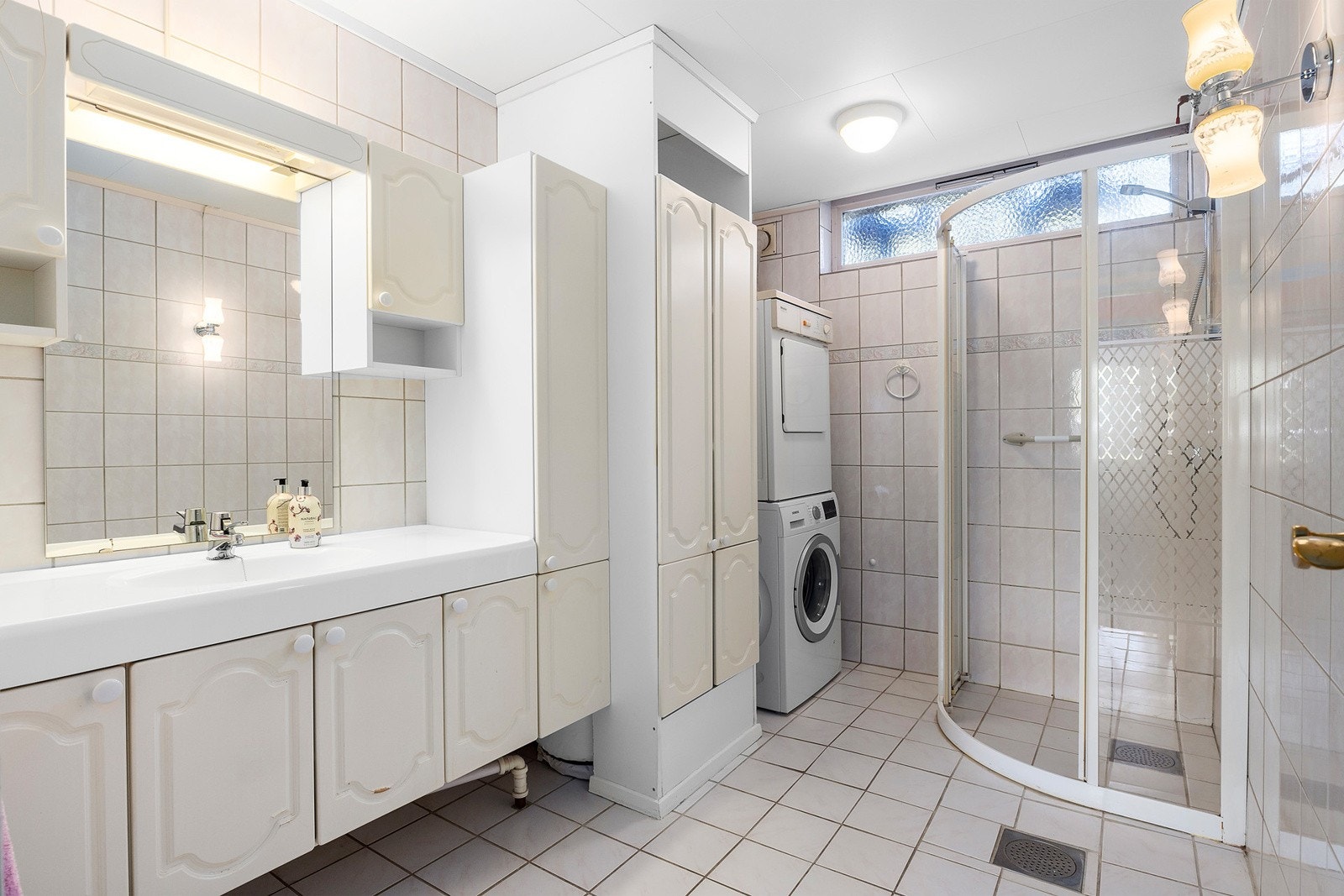 Romslig flislagt bad med dusjkabinett, servantskap og opplegg for vaskemaskin Galleribilde