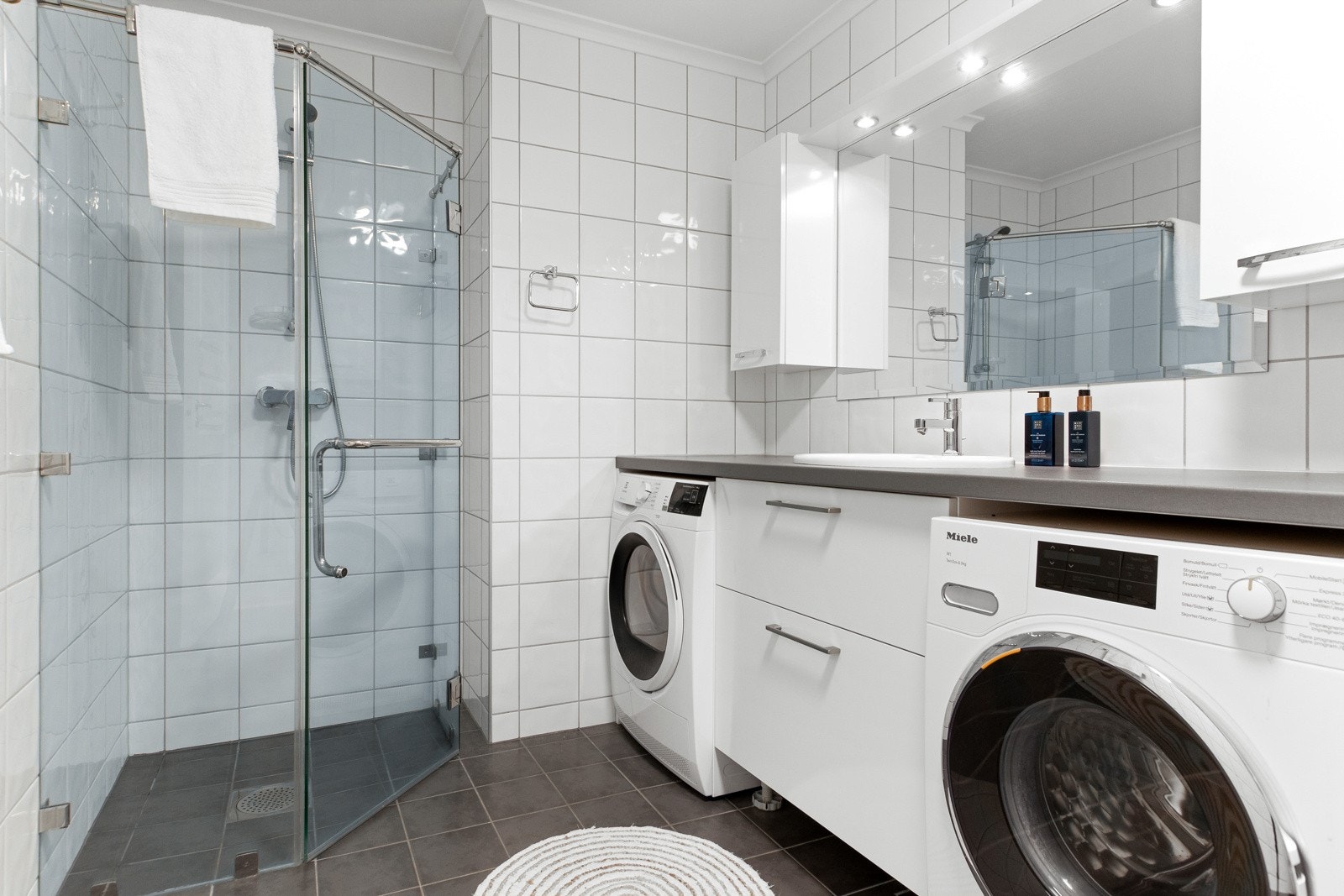 Det er vegghengt toalett og dusjhjørne med veggmontert dusjgarnityr skjermet av dusjvegger og skyvedør i glass. Galleribilde