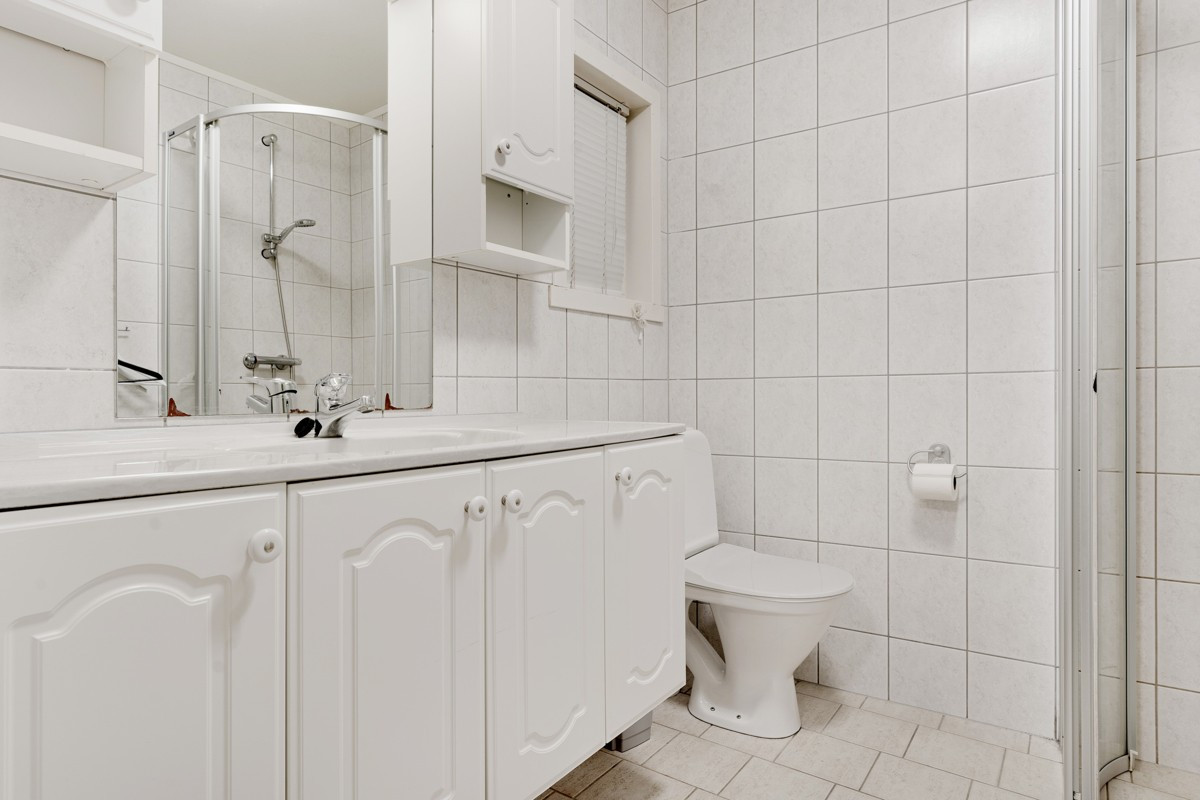 Badet er komplett flislagt med dusjhjørne, gulvmontert toalett og servant m/tilhørende speil og skap