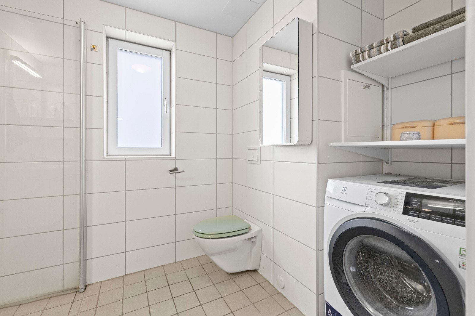 Baderommet er flislagt, med egen nisje for vaskemaskin og praktiske oppbevaringsløsninger Galleribilde