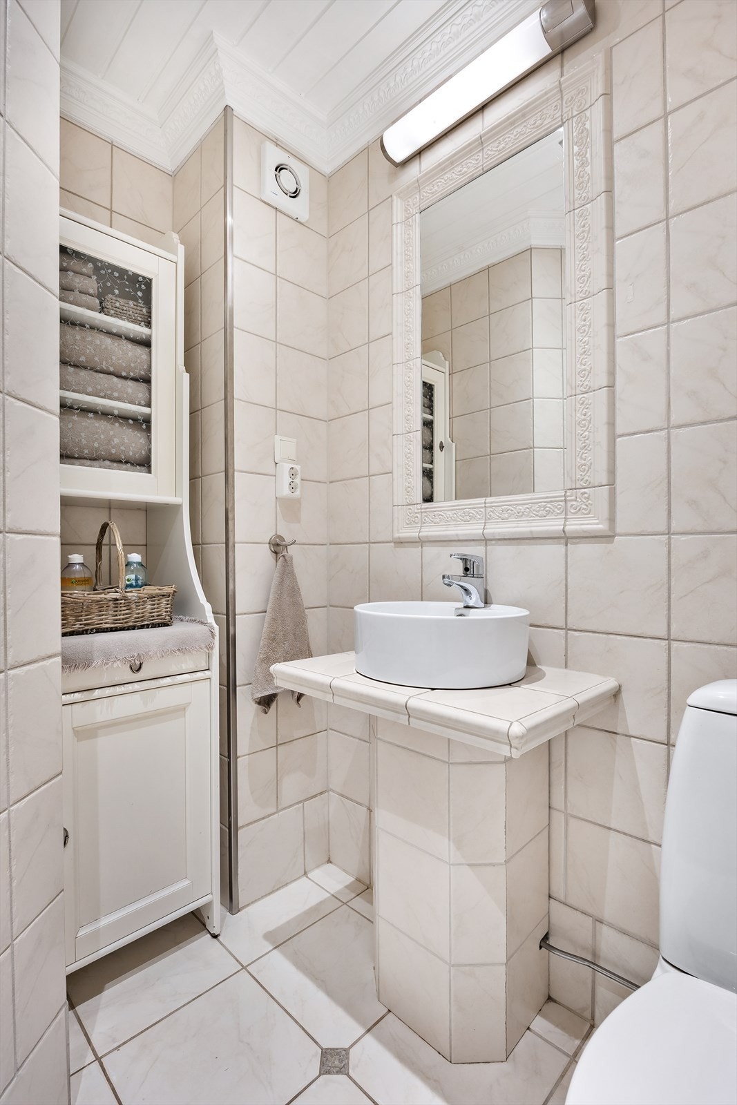 Innredningen består av et hvitt høyskap, et innfelt speil med belysning og en flislagt benkeløsning med toppmontert servantskål. Galleribilde