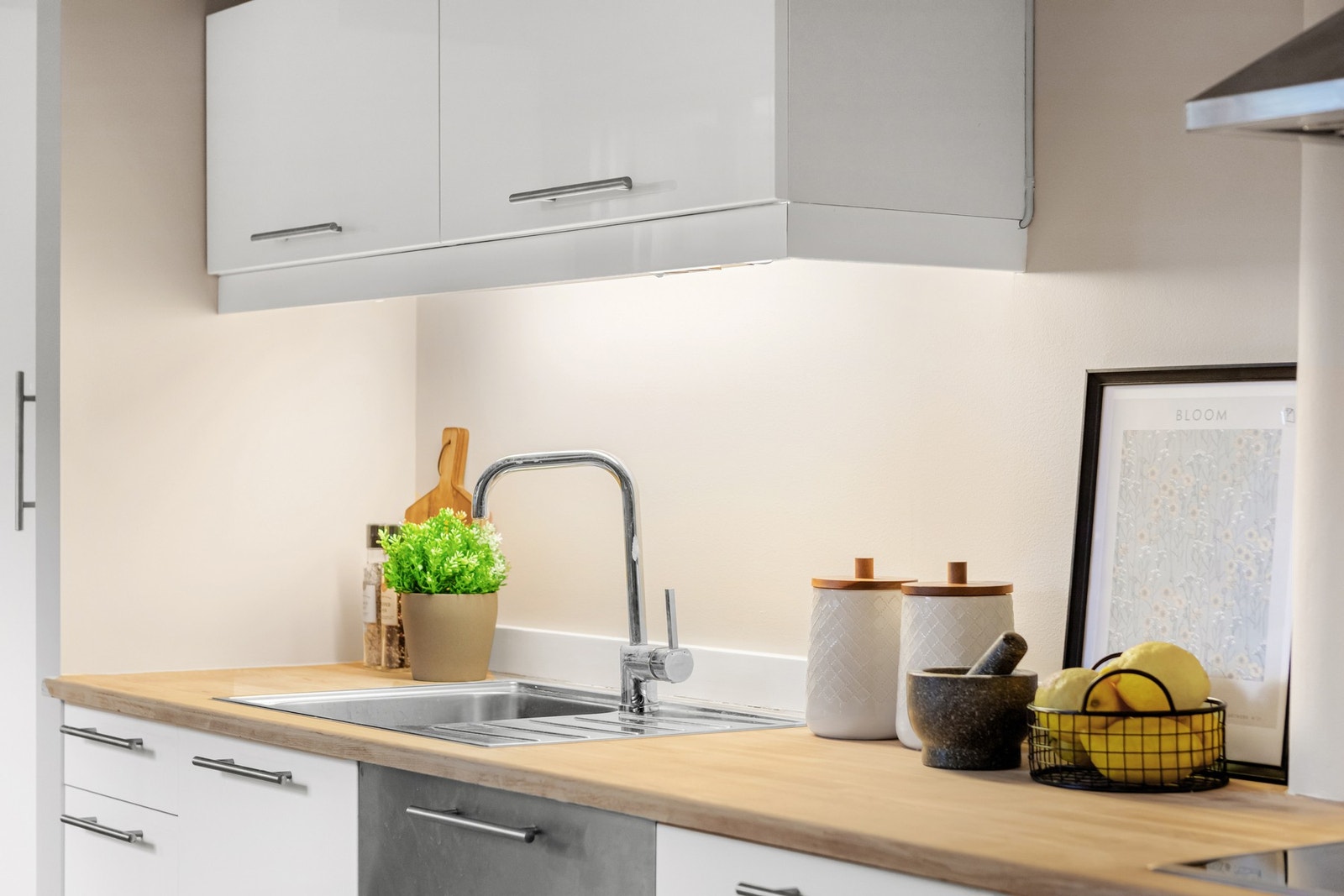 Hvitt klassisk kjøkken med nybeiset heltre benkeplate og nedfelt vaskekum i stål samt lys under overskap Galleribilde