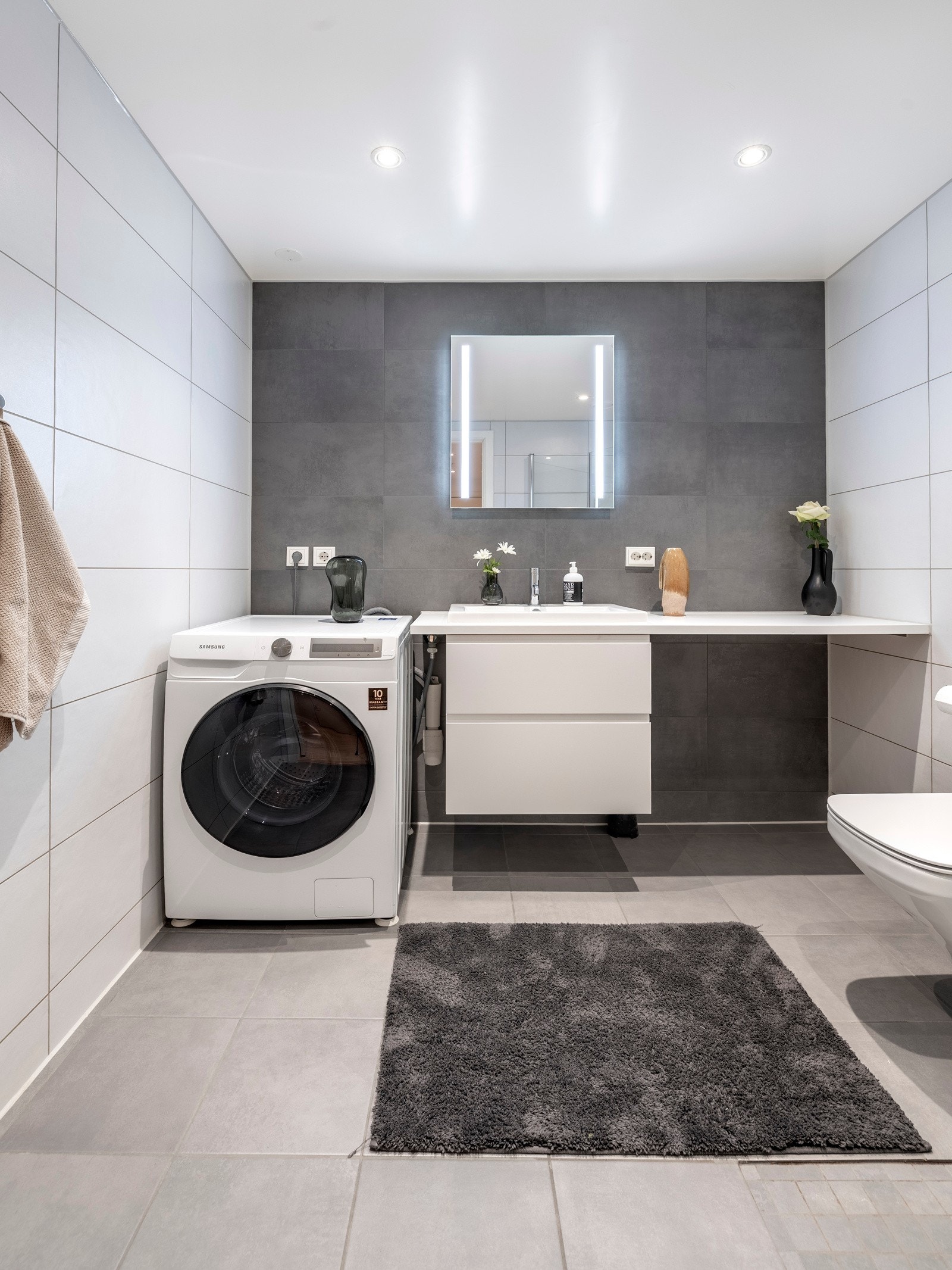 Leiligheten har et lekkert bad, innredet med grå fliser på gulv, lyse fliser på veggene, og én vegg med mørkegrå fliser som gir et elegant kontrastpreg. Galleribilde