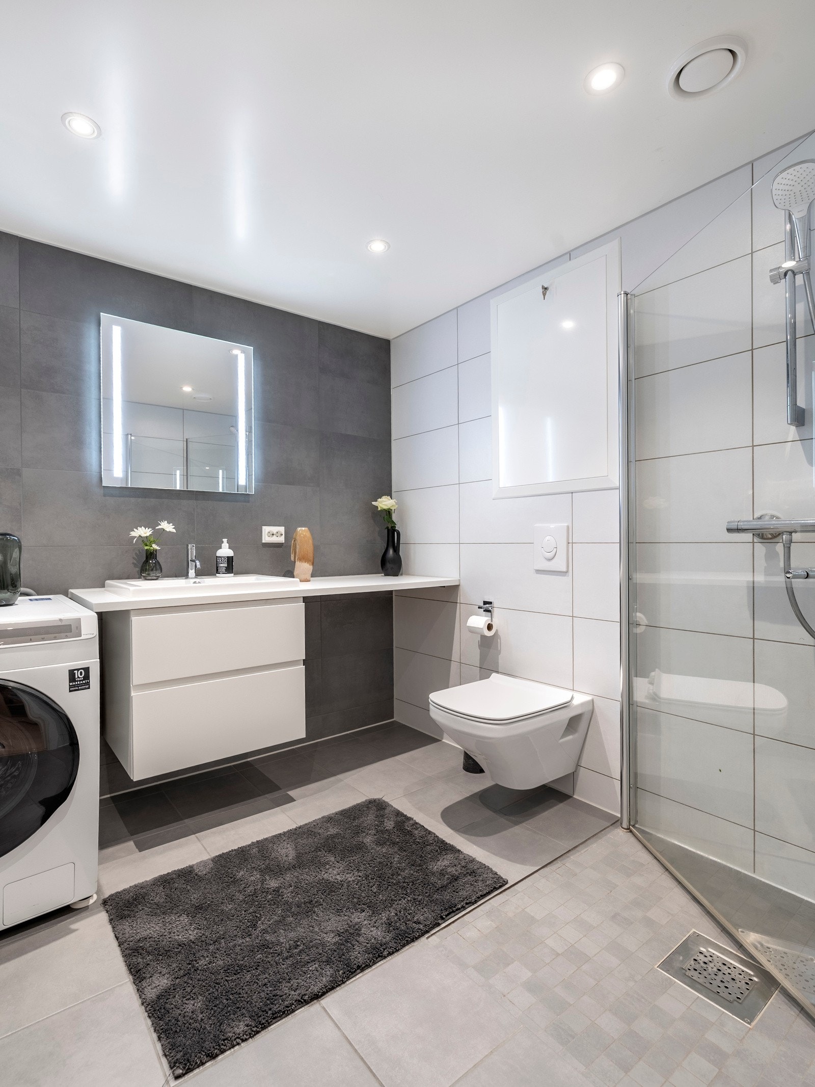 Det er vannbåren varme i gulvet og downlights i himlingen, som skaper en lys og moderne atmosfære. Badet er også utstyrt med praktisk opplegg for både vaskemaskin og tørketrommel, som gir ekstra funksjonalitet. Galleribilde