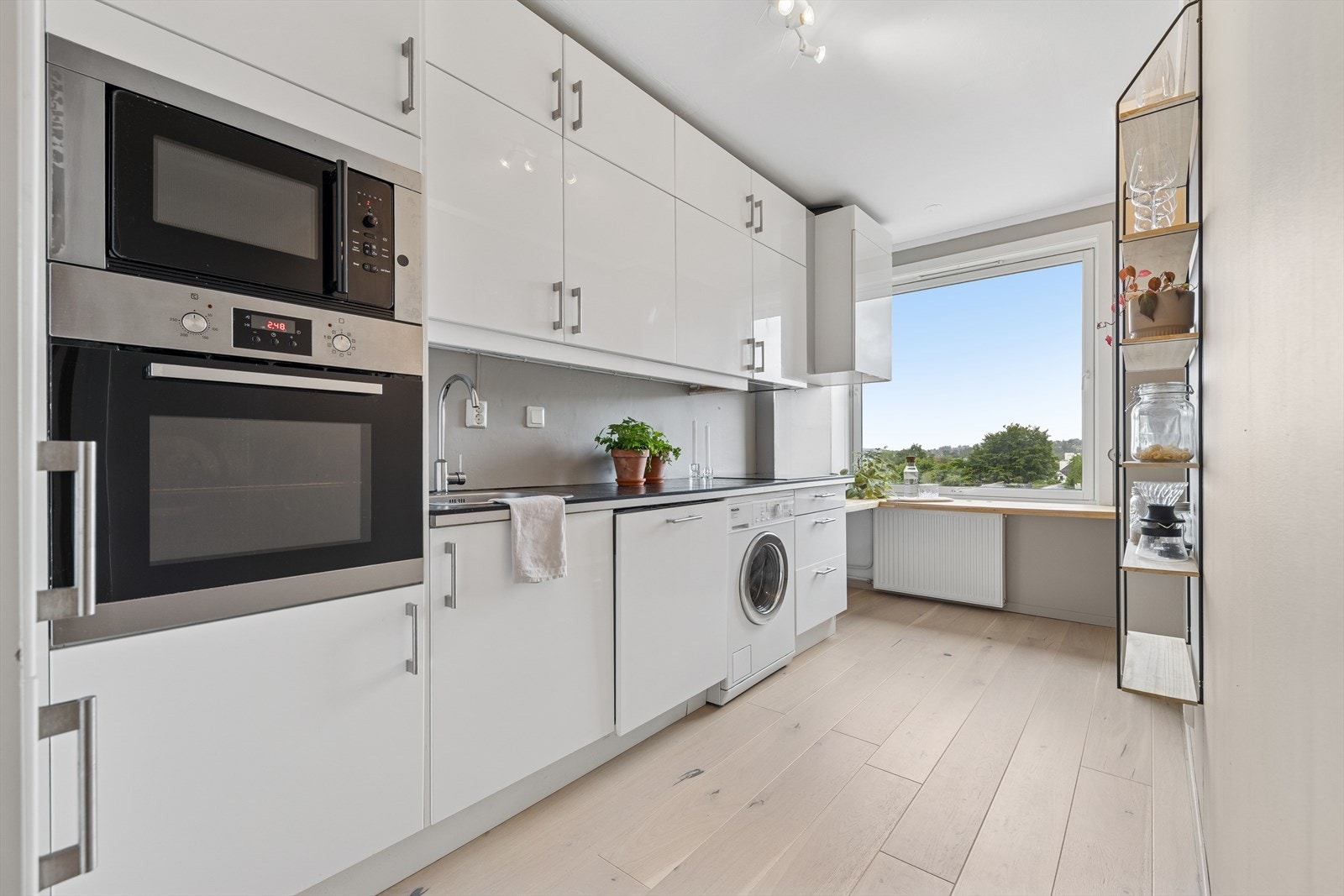 Kjøkkeninnredningen har lyse fronter og ekstra høye overskap, noe som gir både et moderne uttrykk og ekstra lagringsplass. Det er godt med benkeplass, og kjøkkenet er utstyrt med opplegg for vaskemaskin Galleribilde