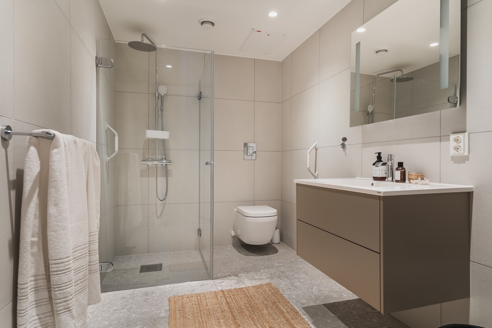 Badene har også speil med belysning over servant som er tilpasset bredden på innredningen - Det er dusj på gulv med dører i herdet glass og regnfallsdusj samt veggfestet klosett med innebygget sisterne Galleribilde