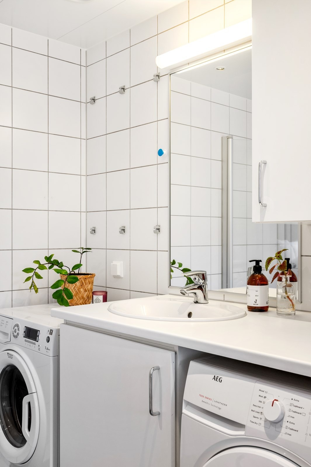 Videre har badet dusjhjørne med glassdører og veggmontert dusjarmatur, vegghengt toalett med innebygget sisterne og opplegg for vaskemaskin og tørketrommel. Avtrekksventil plassert i himling. Galleribilde