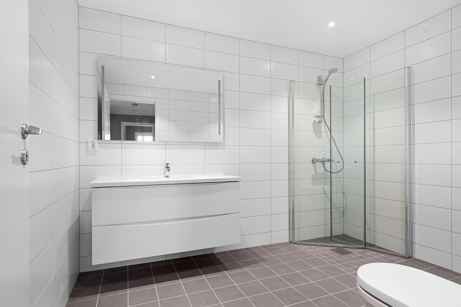 Bad/wc leveres med 120 cm servantmøbel og speil med belysning. Vegghengt toalett. Dusjhjørne med dusjvegger på 90 cm x 90 cm i klart glass med blanke profiler og LED downlights i tak Galleribilde